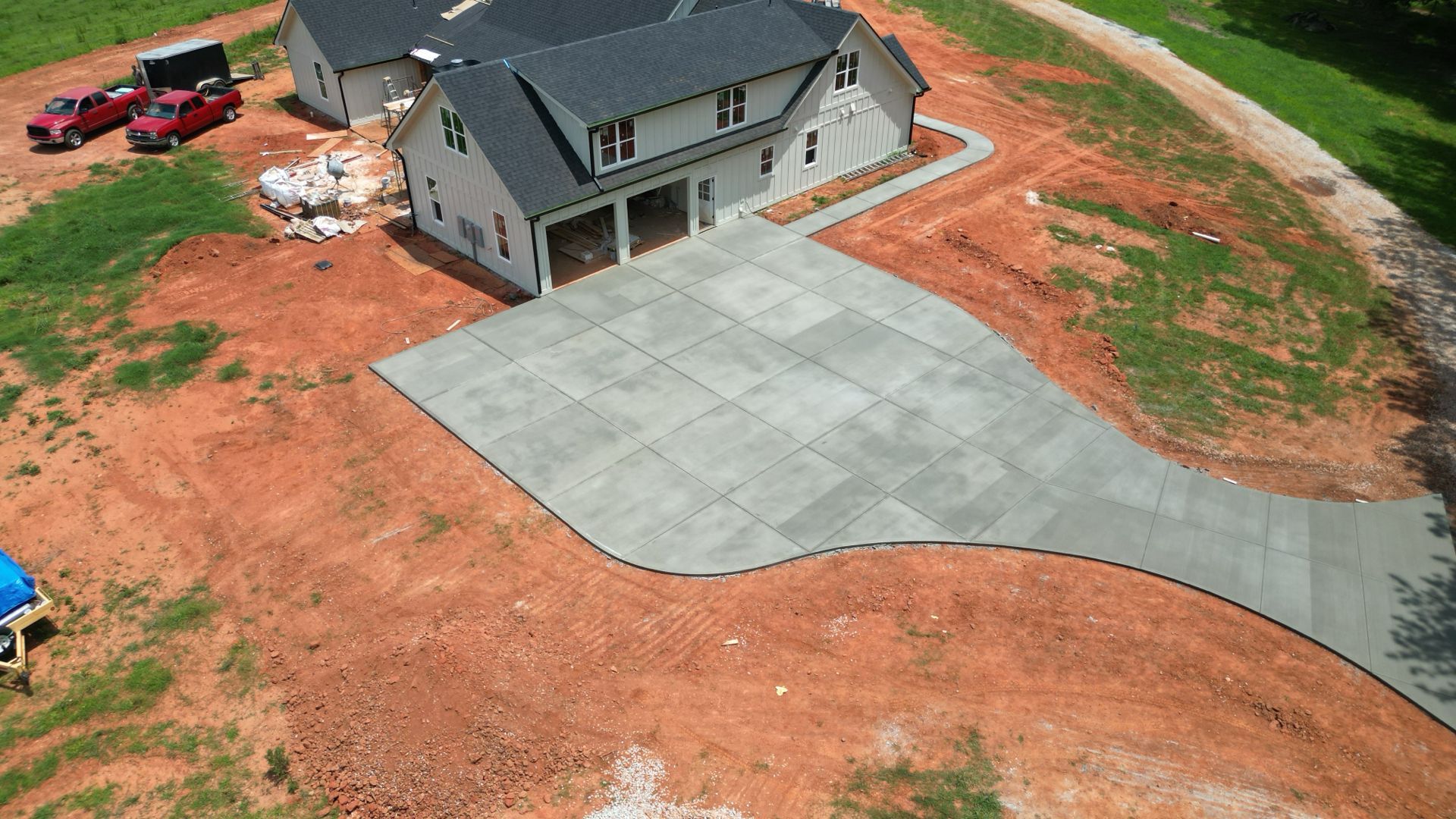 Aerial view of a house with a large concrete driveway and red dirt yard, with a red truck nearby.