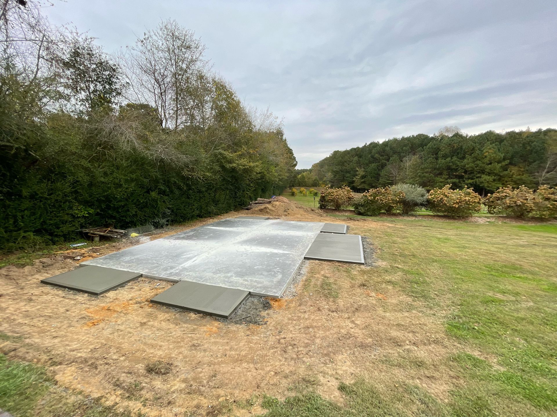 Outdoor metal platform or ramp on a grassy field beside dense trees and shrubs