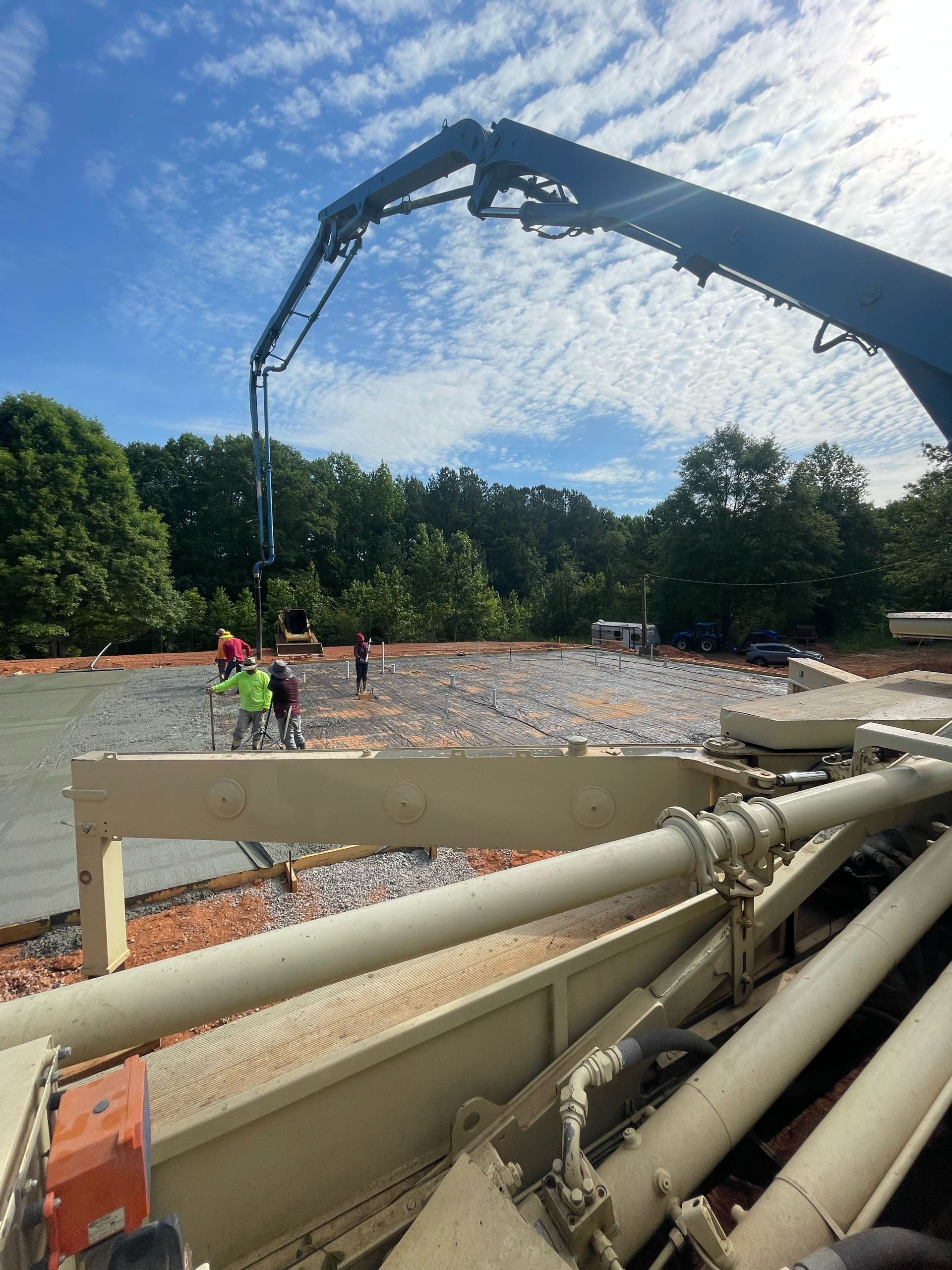 Concrete pump pouring a slab at a construction site, with workers and a boom arm under a blue sky