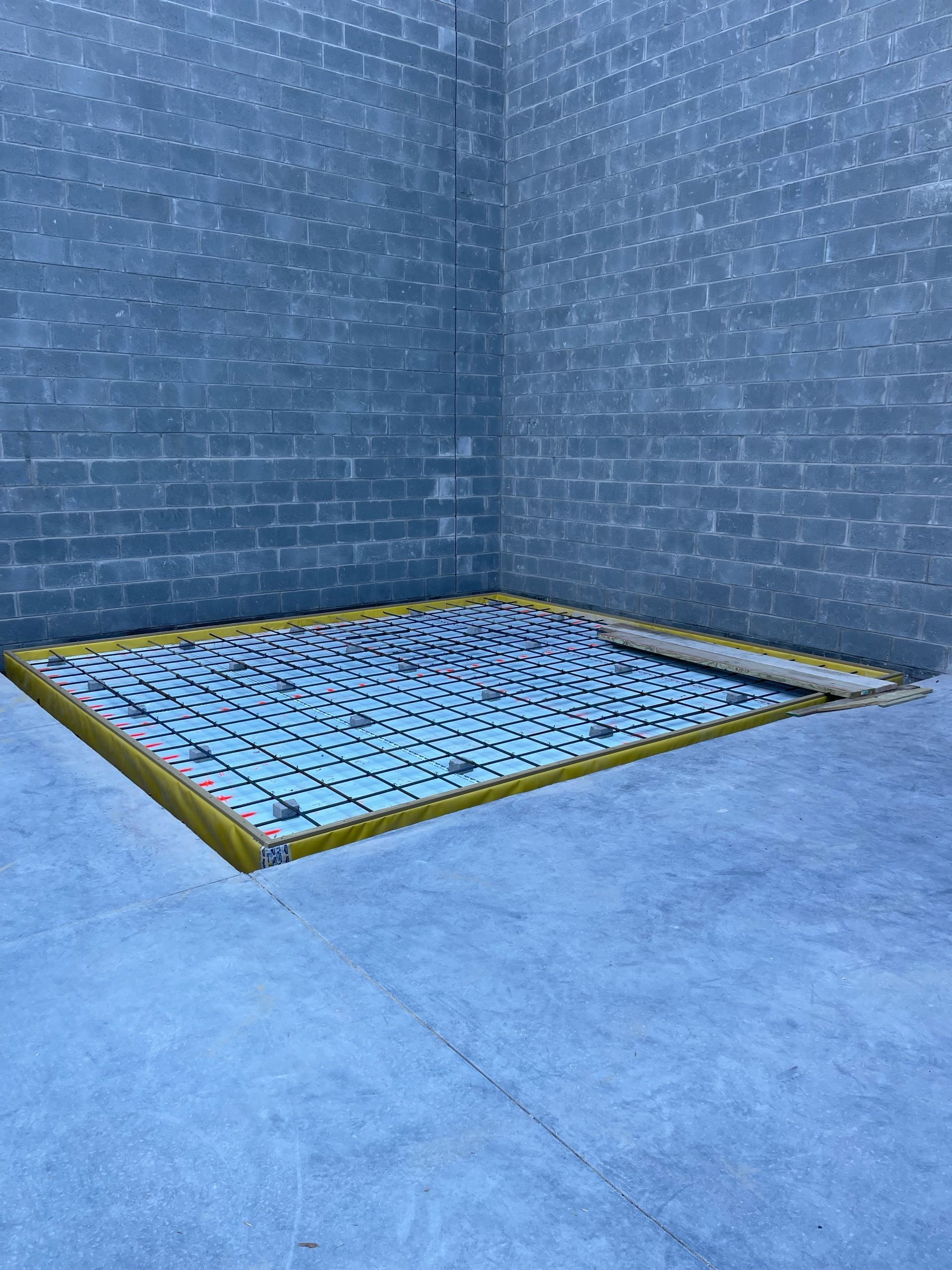 Blue tiled corner with a recessed metal grate in the floor, surrounded by a yellow border.