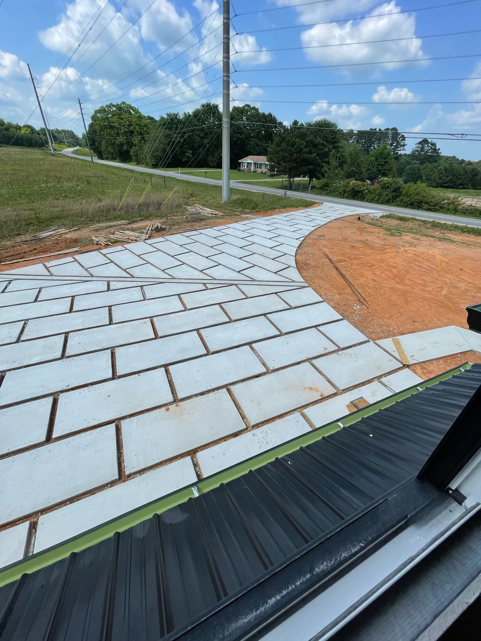 Paved walkway with white pavers, orange dirt, and a roadside view under a cloudy sky