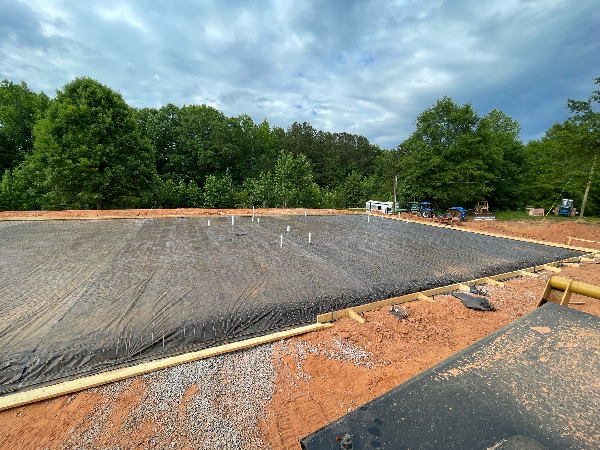 Freshly paved parking lot with gravel edge, orange dirt, and trees under a cloudy sky