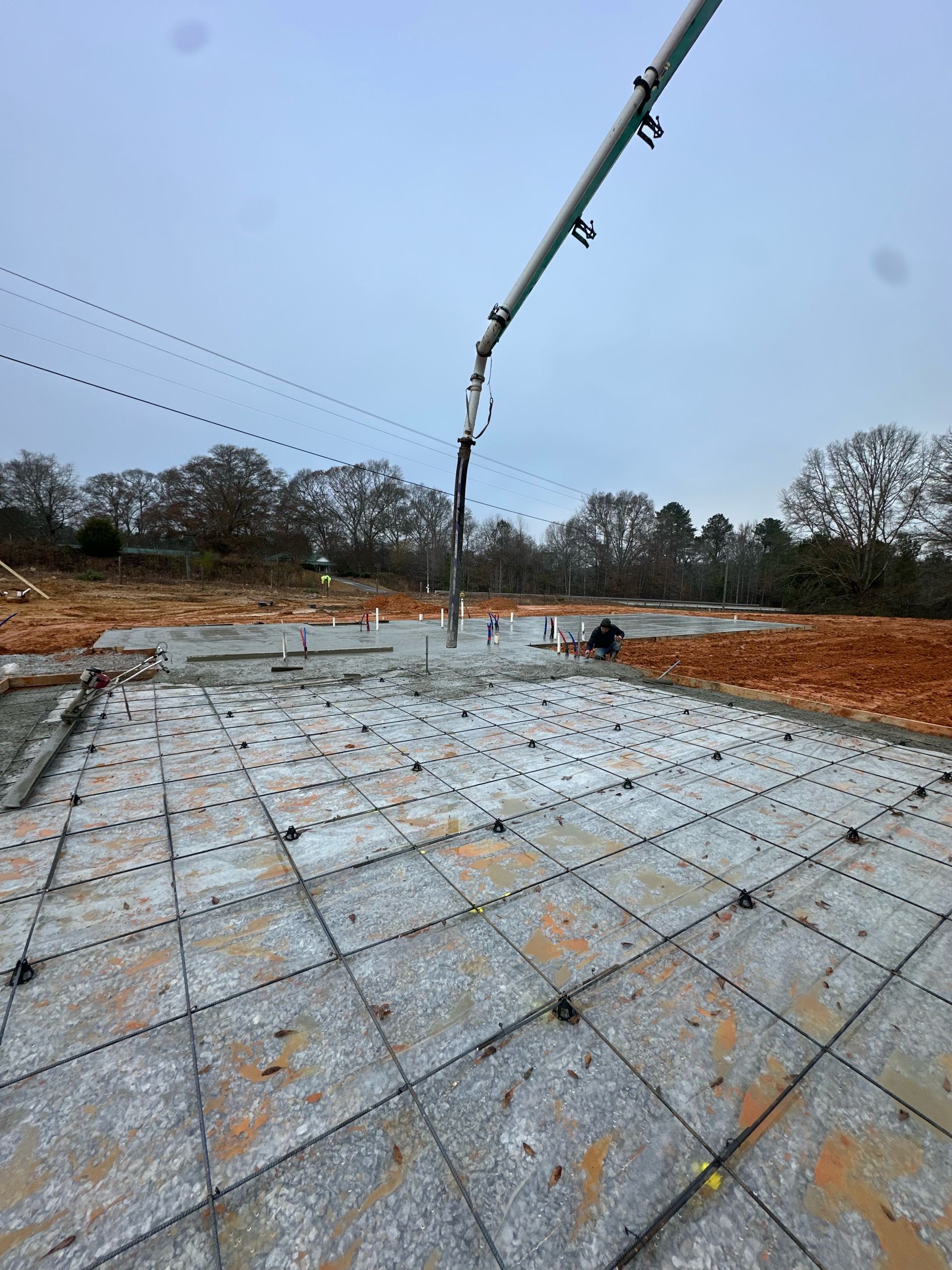 Concrete foundation slab under construction with a pump boom pouring wet concrete on a cloudy day