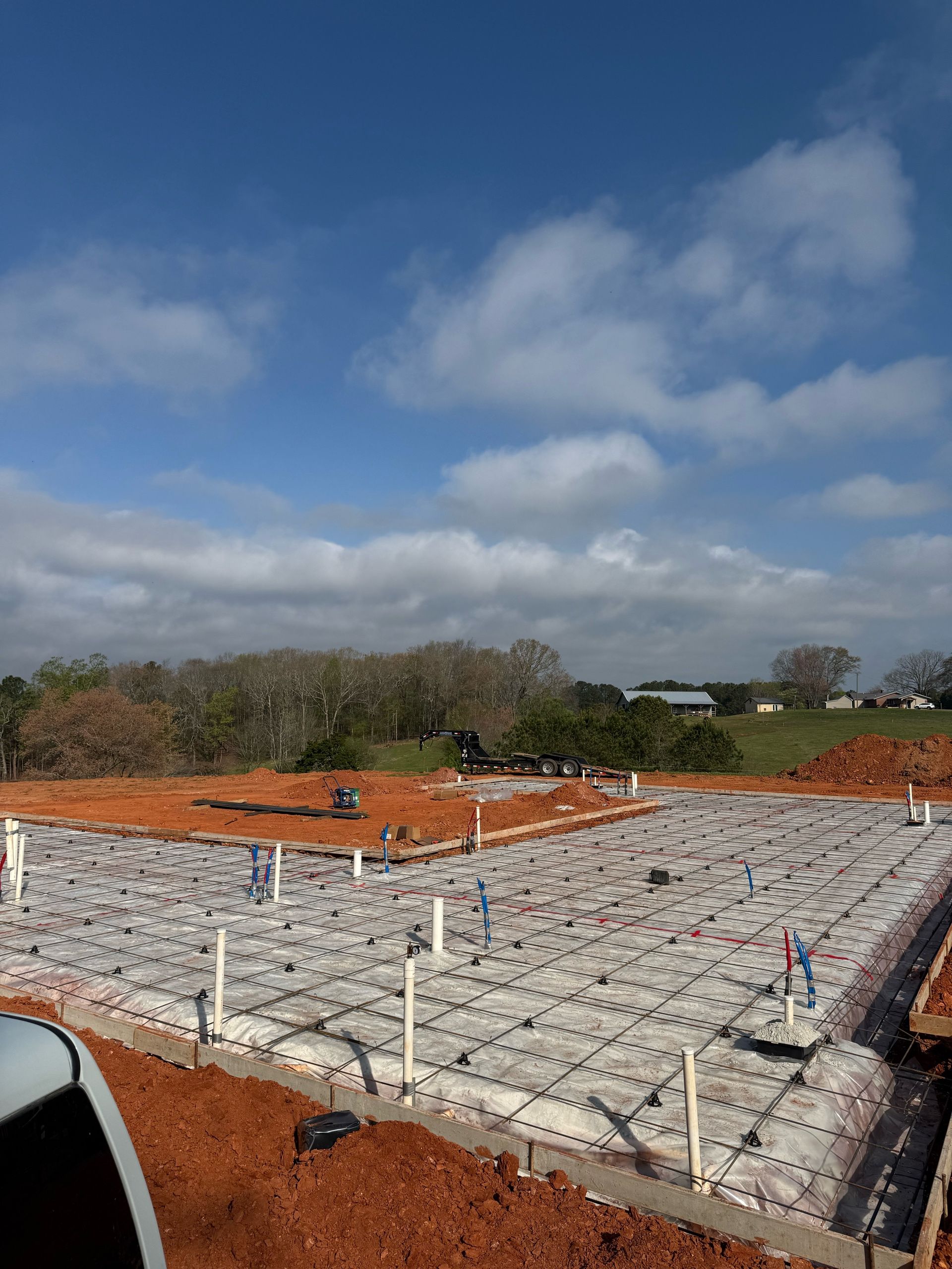 Rooftop under construction with orange insulation and white beams beneath a cloudy blue sky.