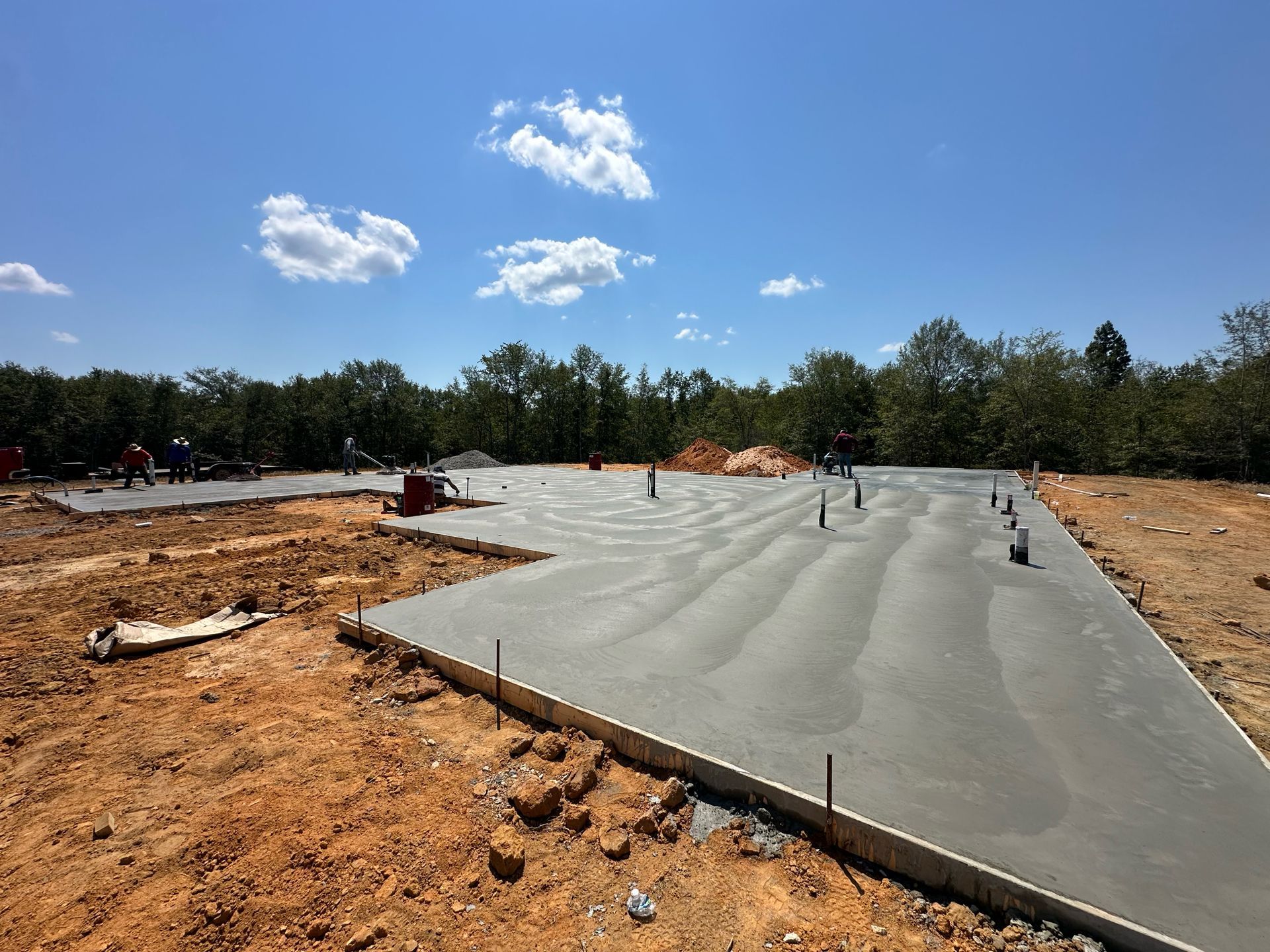 Concrete foundation slab being poured at a construction site under a blue sky.