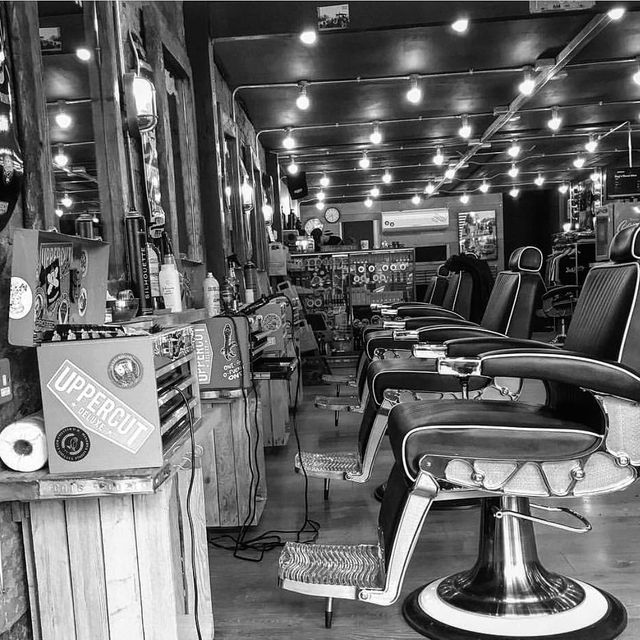 A black and white photo of a barber shop with a lot of chairs.