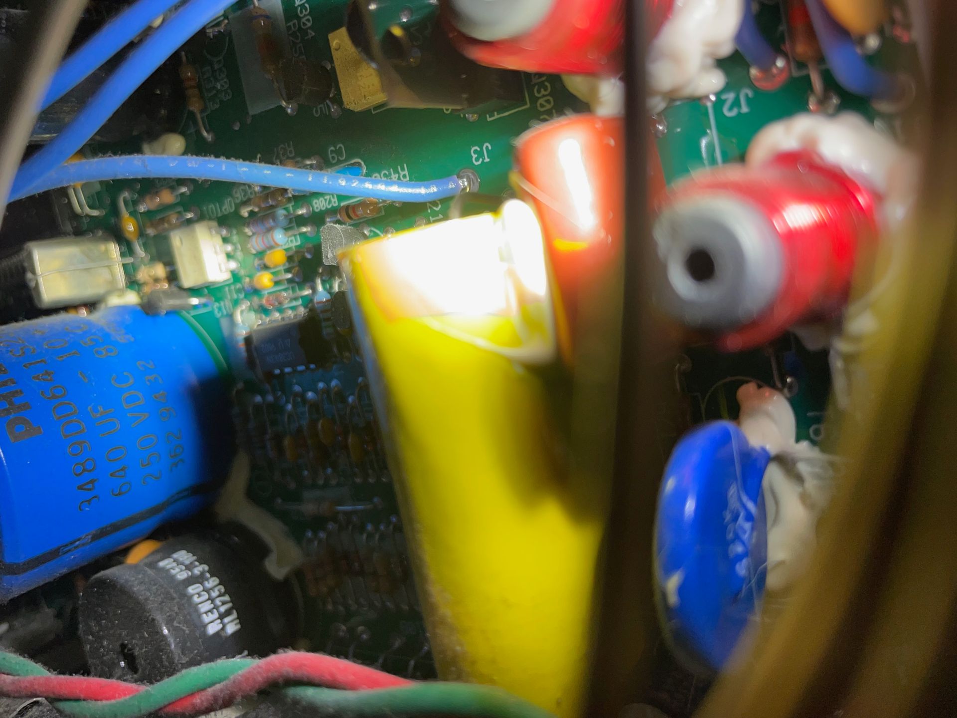 Close-up of electronic components inside a device. Yellow, red, blue, and black capacitors and wires are visible on a green circuit board.