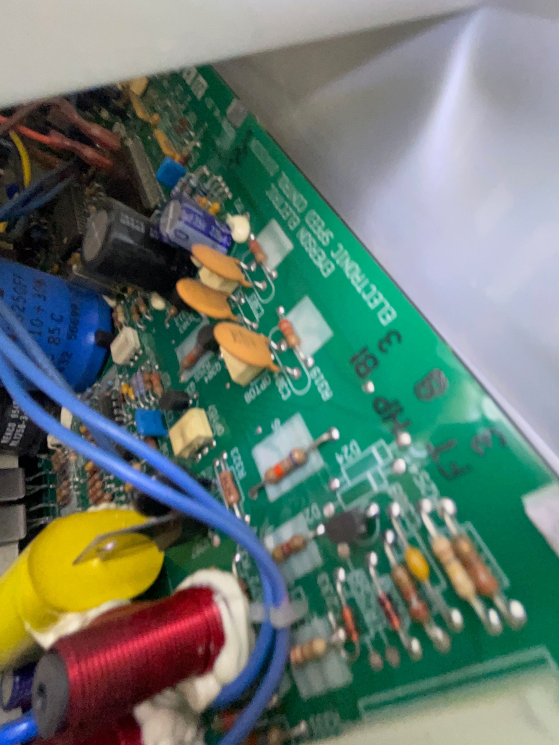 Green circuit board with electronic components, including capacitors, resistors, and blue and yellow wires. Text reads 