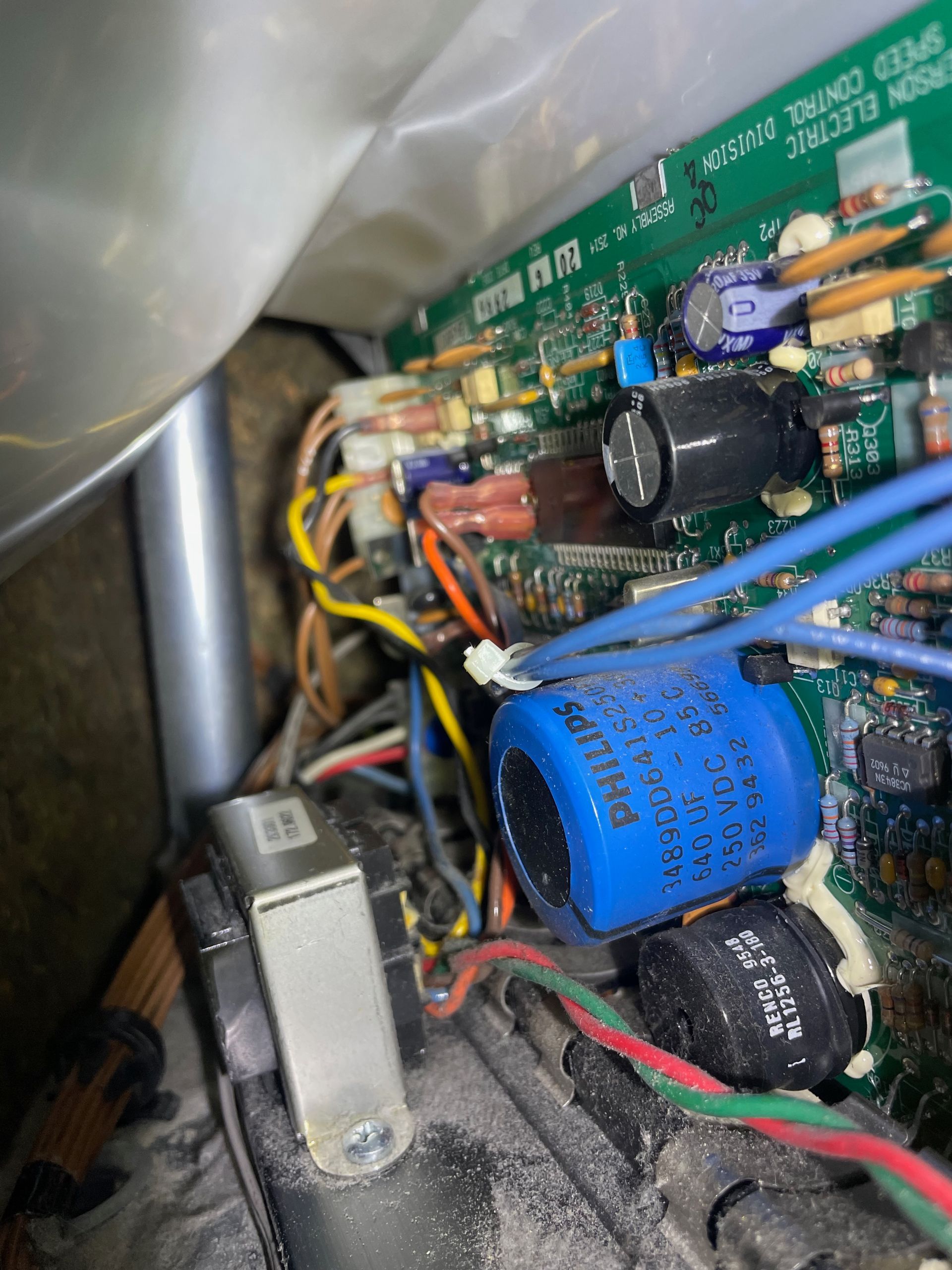 A close-up of a treadmill's circuit board, showing wires, capacitors (blue, black), and electronic components.