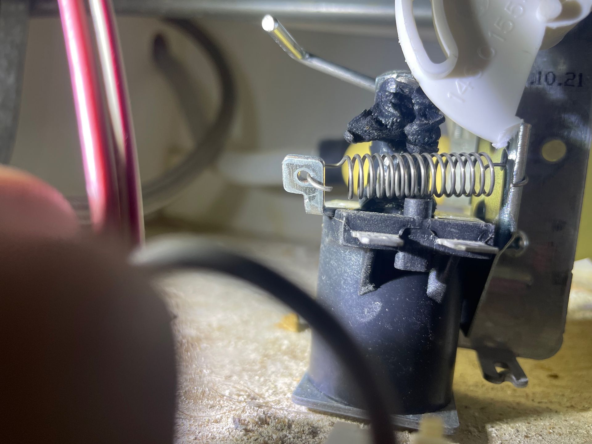 Close-up of a furnace component with a burned-out heating element and wires. Black, gray, and white components are visible.