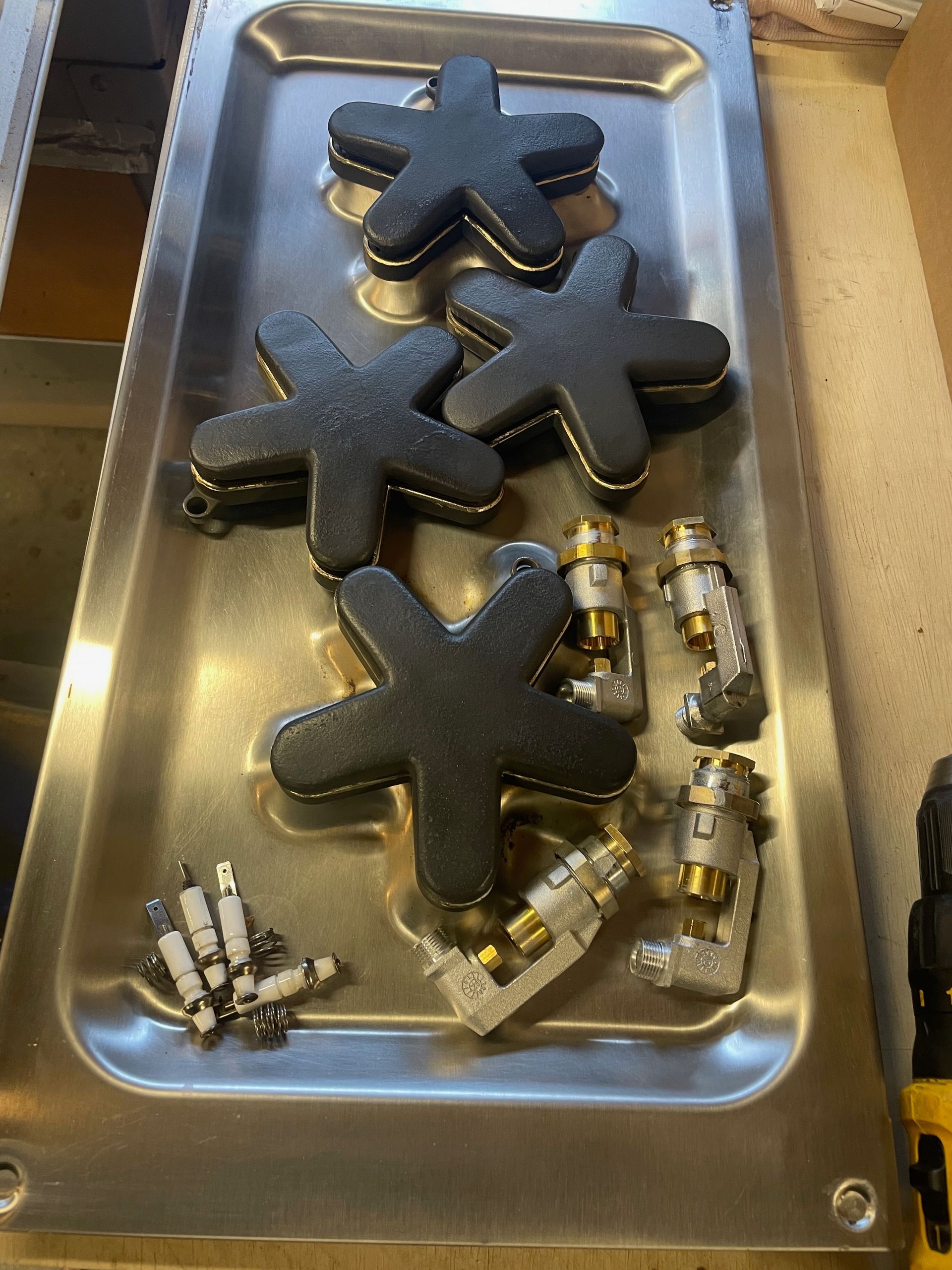 A metal tray holds three black, star-shaped stove burners, along with gas valve components.