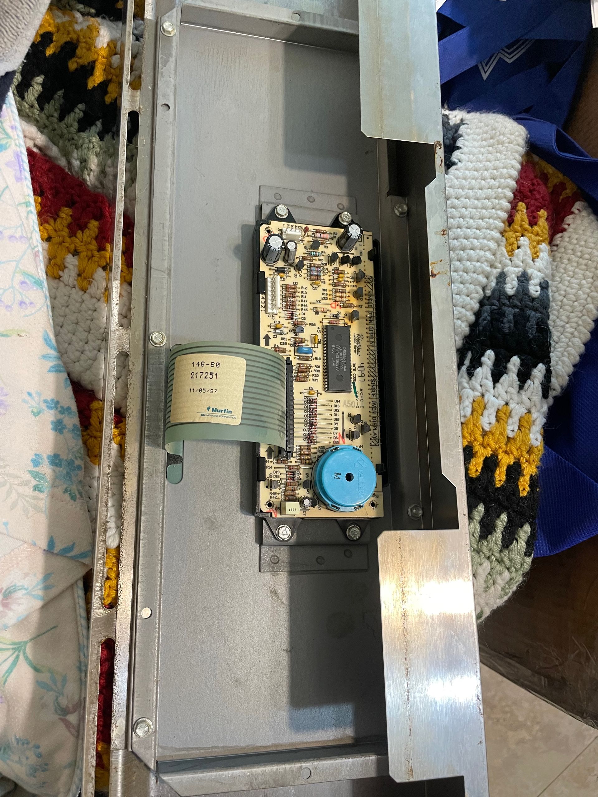 Electronic circuit board inside a metal frame. A beige transformer and a blue dial are also visible.