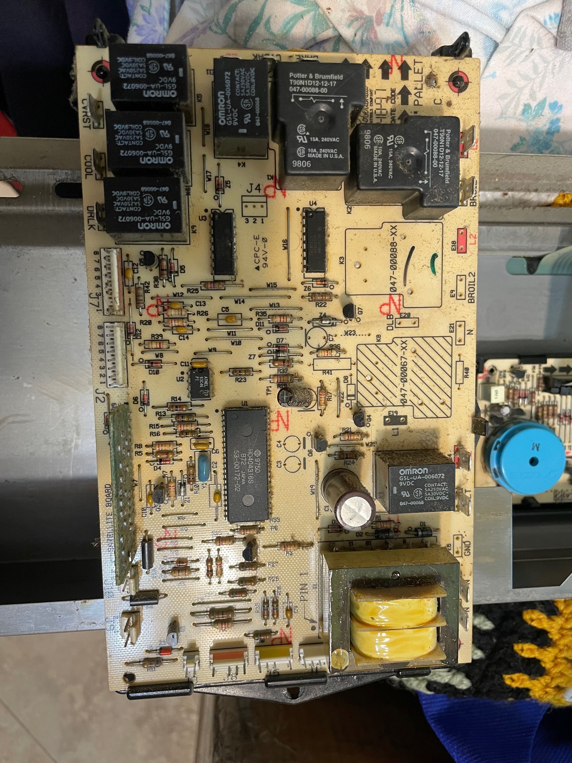 Printed circuit board with several black relays and integrated components on a beige background. It appears to be electronics from an appliance or machine.