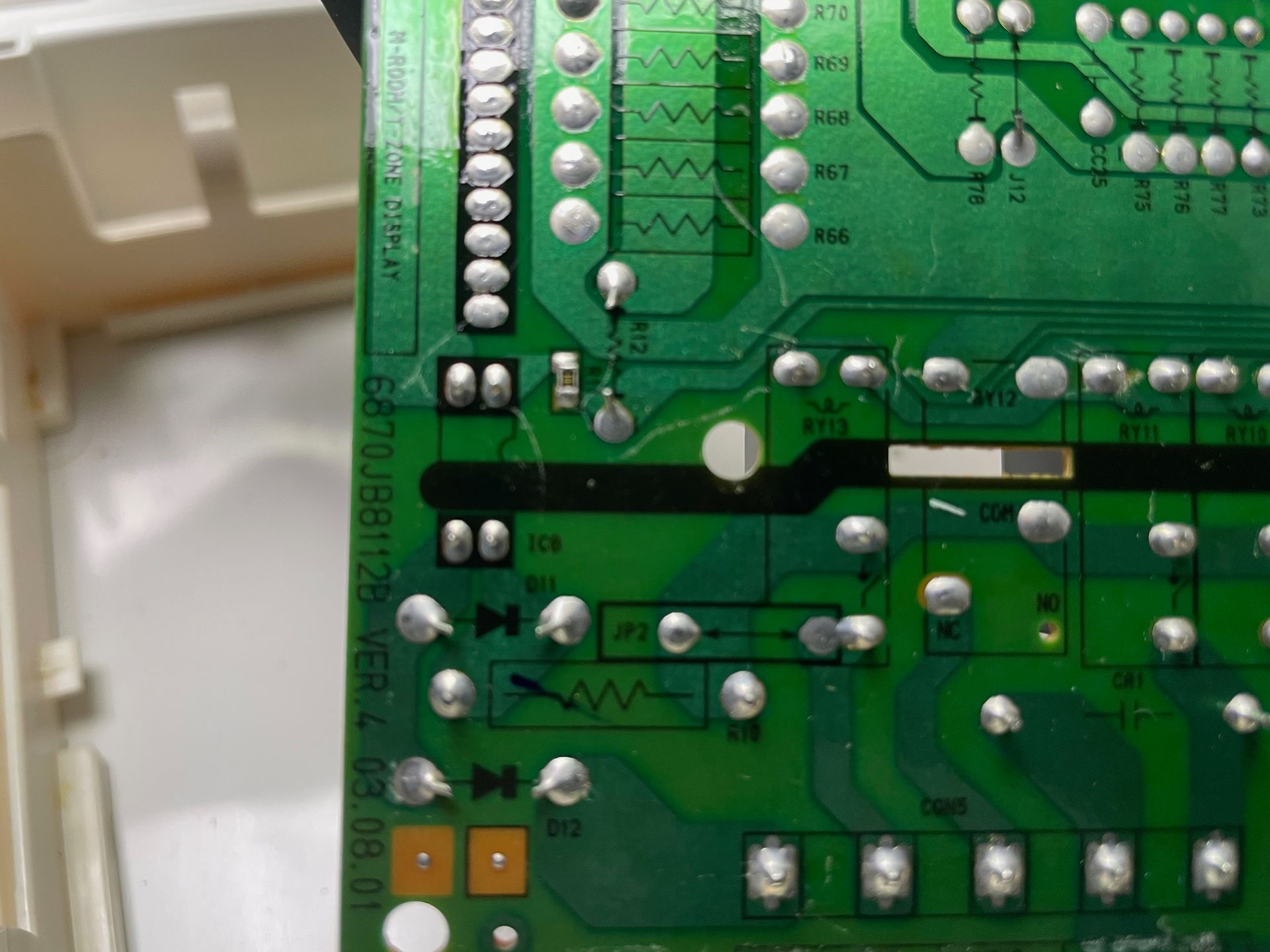 Green circuit board close-up with silver solder points, various components, and traces, possibly from an electronic device.