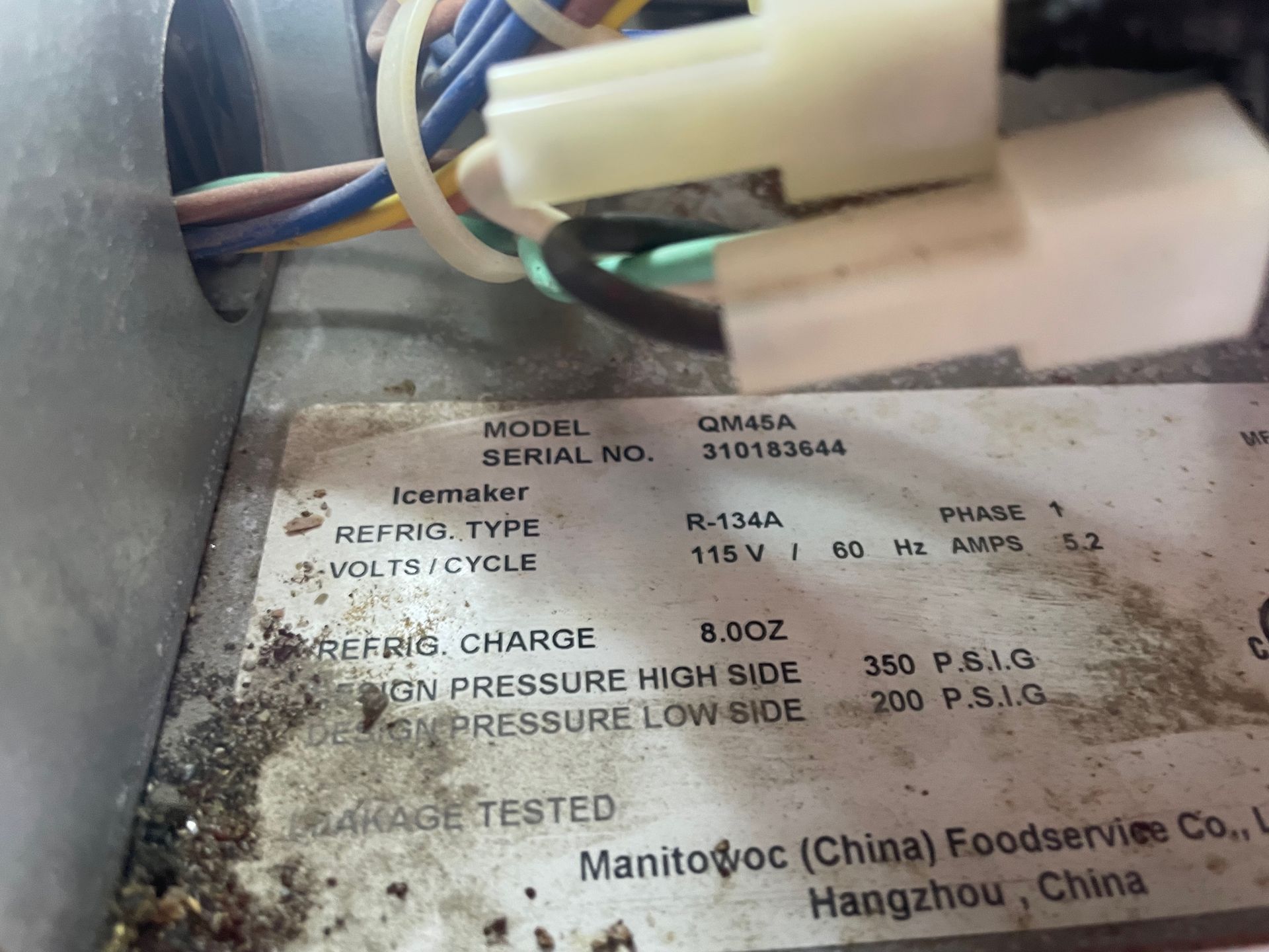 Close-up of an icemaker label with model and specifications, including refrigerant type R-134A, and manufacturer details.