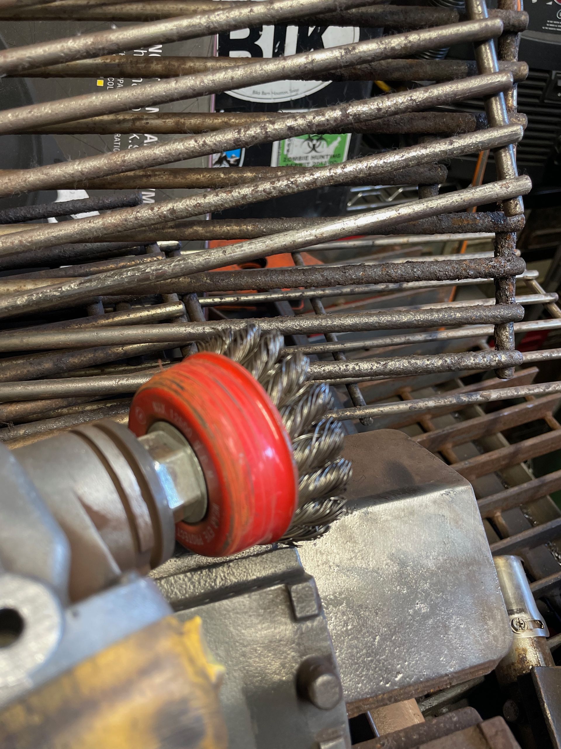 A person using a wire brush attachment on a grinder to clean metal bars, likely in a workshop. The brush is red.