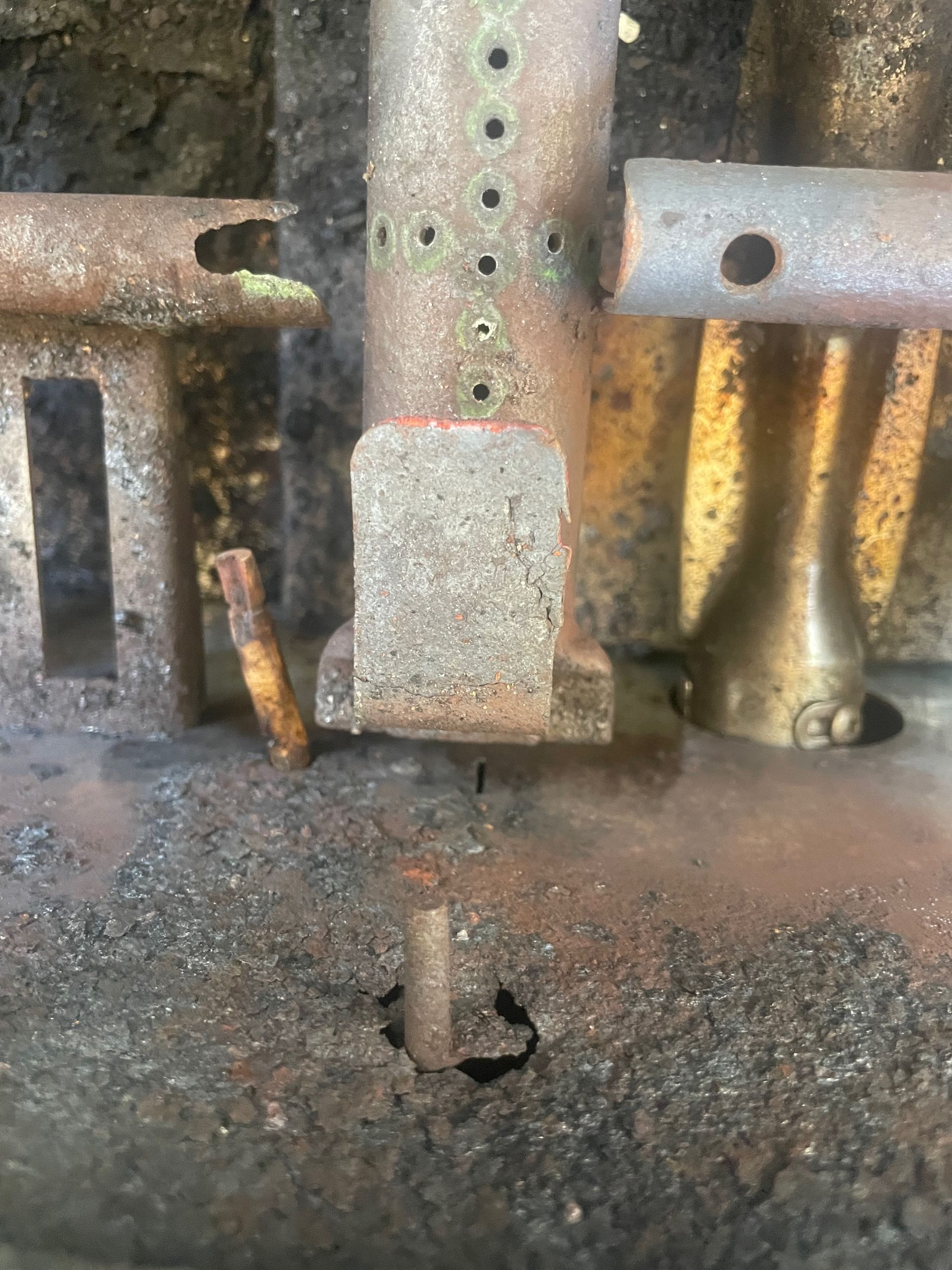 Close-up of a rusty gas grill burner assembly. Various metal components are visible, with signs of wear and corrosion.