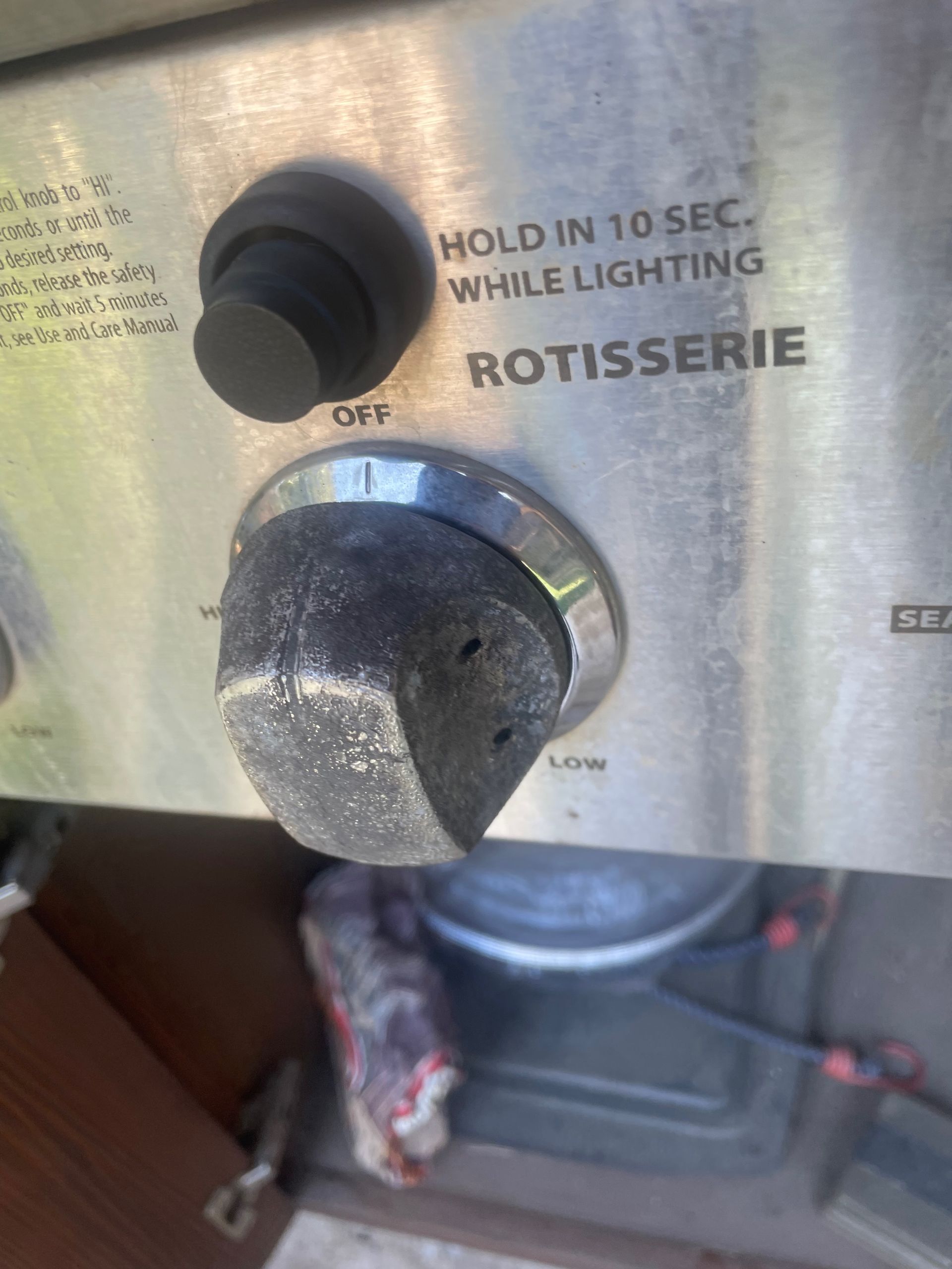 Close-up of a stainless steel grill control panel. It shows a black and silver rotisserie knob with 