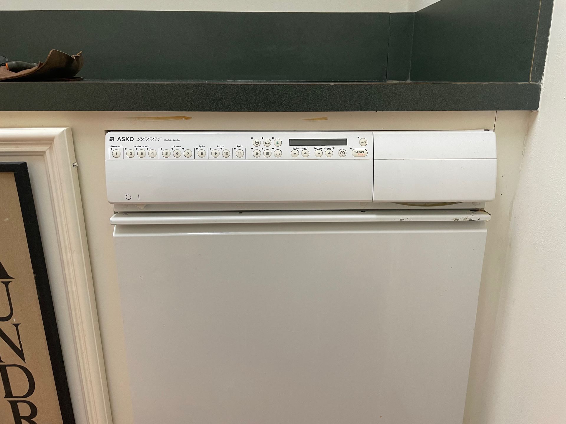 White dishwasher built into a kitchen cabinet. The control panel has buttons and a display.