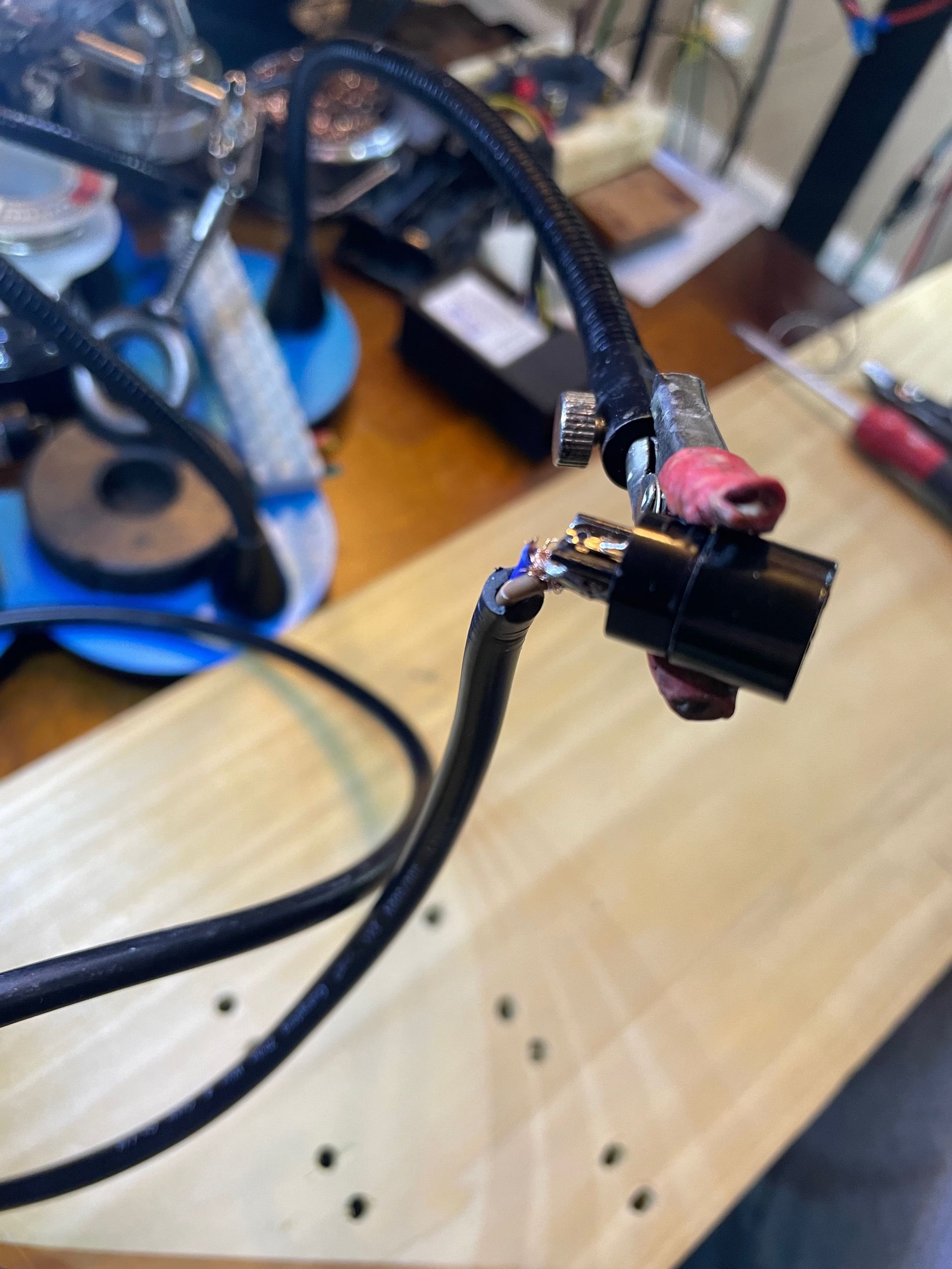 Black cable with a damaged connector, revealing wires, lies on a wooden surface. Soldering tools are visible in the background.