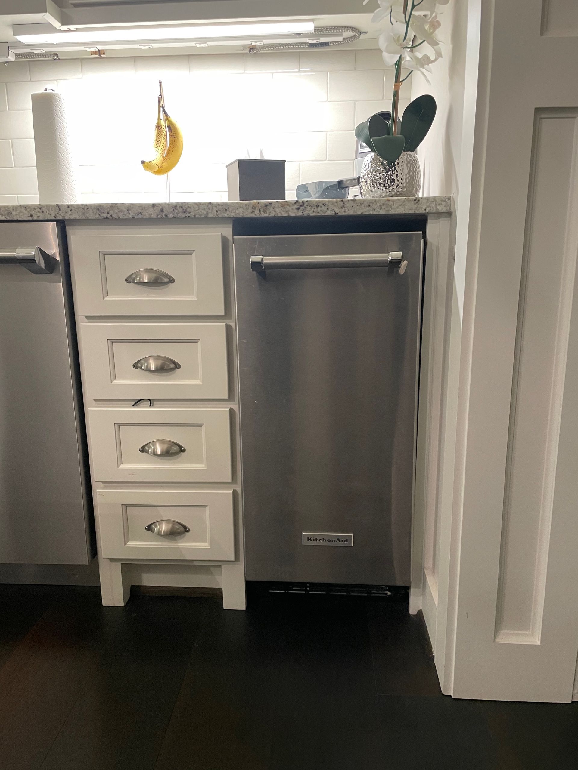 Kitchen with white cabinets, stainless steel dishwasher, and granite countertop. A banana hangs by the window.