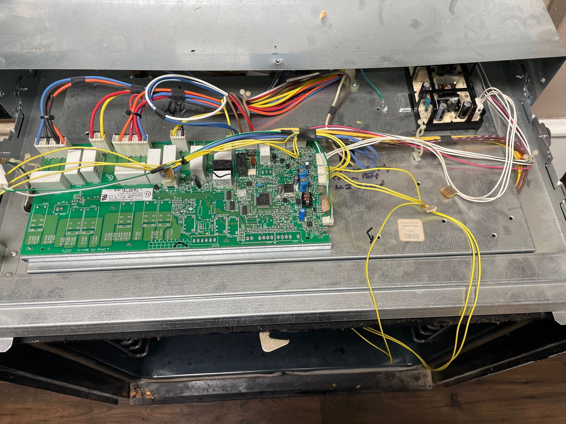 Open oven interior with a green circuit board and various colored wires. The oven housing is metal.