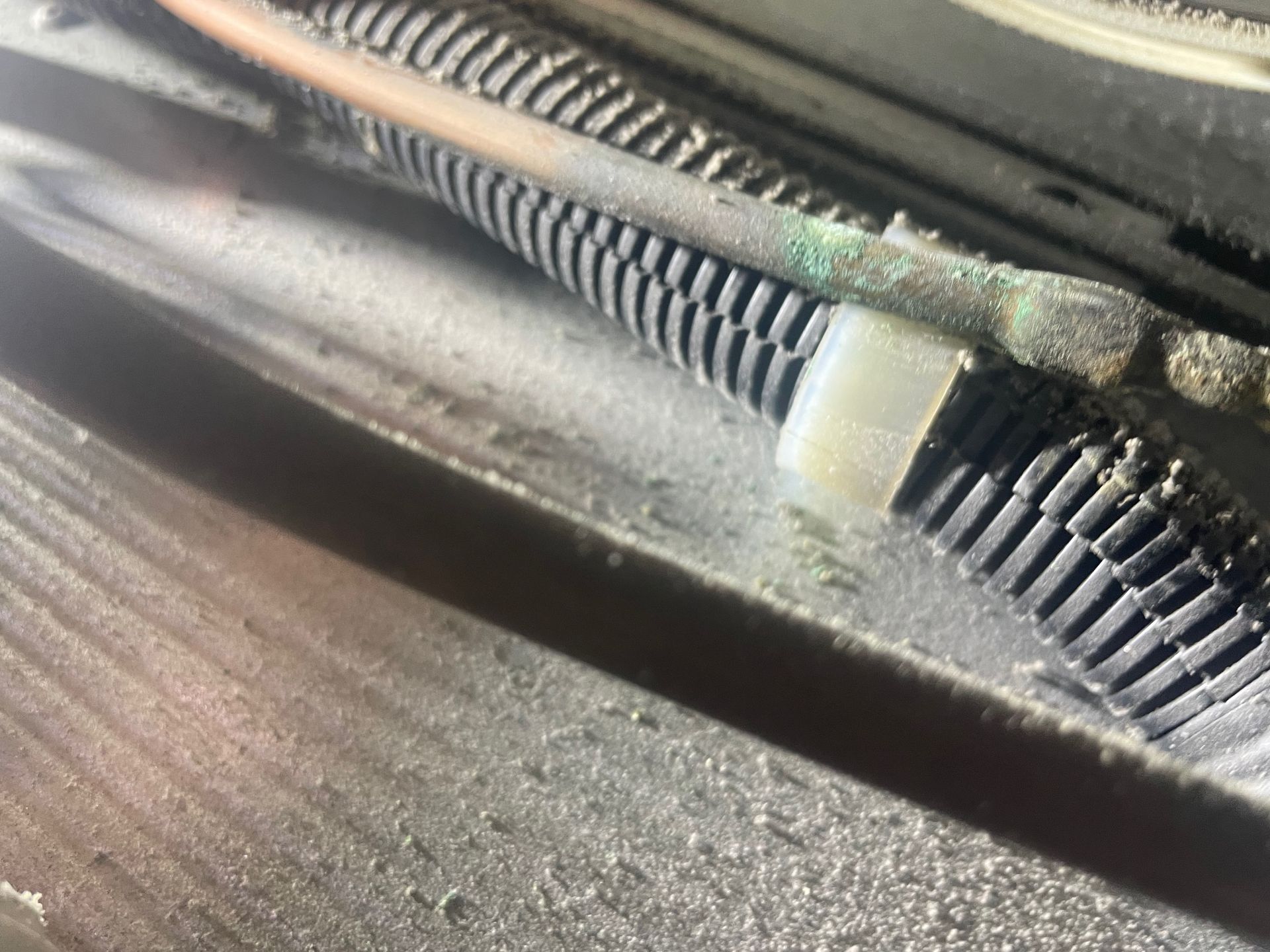 Close-up of a copper tube and a black corrugated tube secured with a white zip tie. The components are covered in dust.