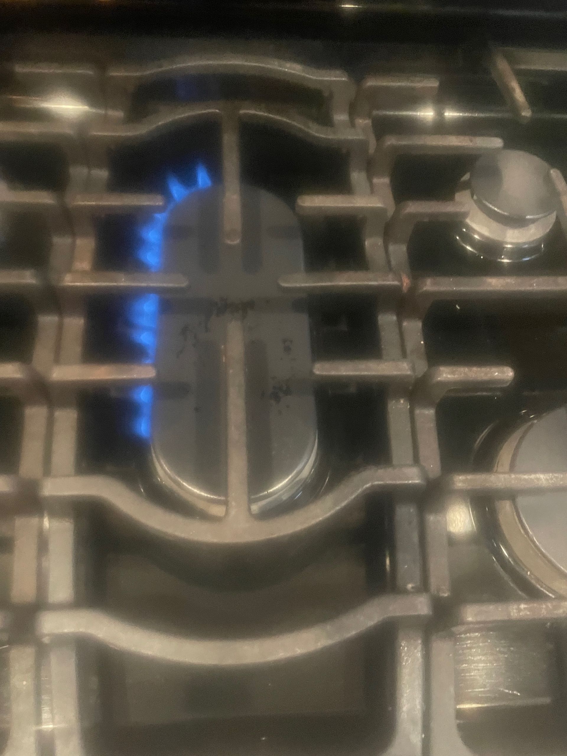 Close-up of a gas stove burner with blue flames lit, surrounded by metal grates and knobs.