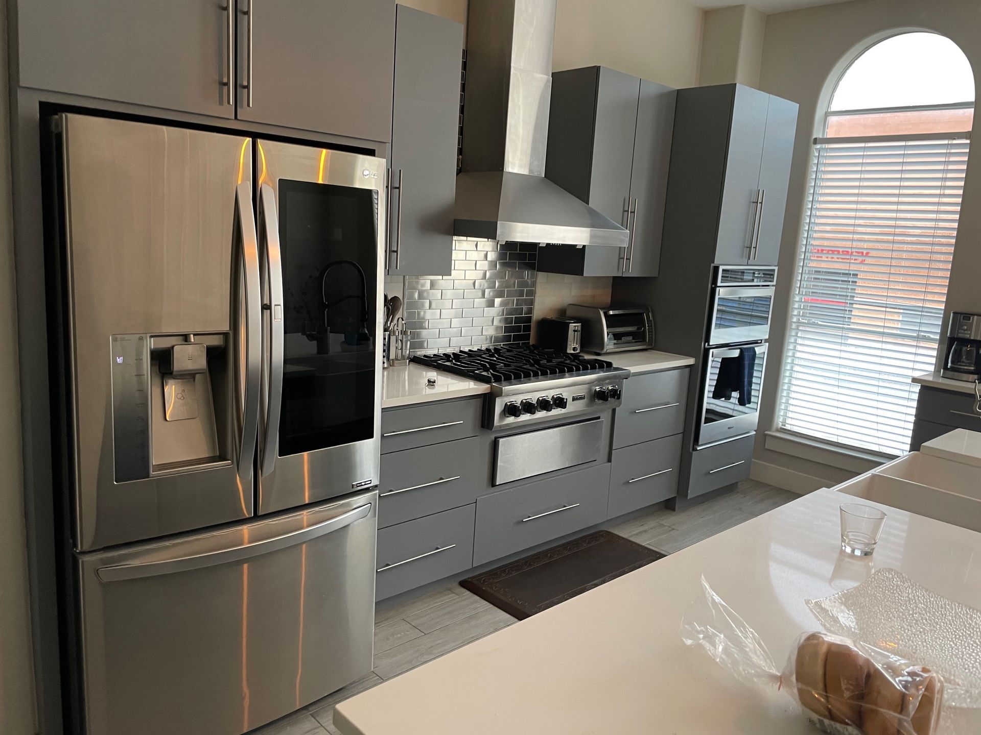 Modern gray kitchen with stainless steel appliances and a white countertop island.  A large refrigerator, oven, and cabinets are visible.