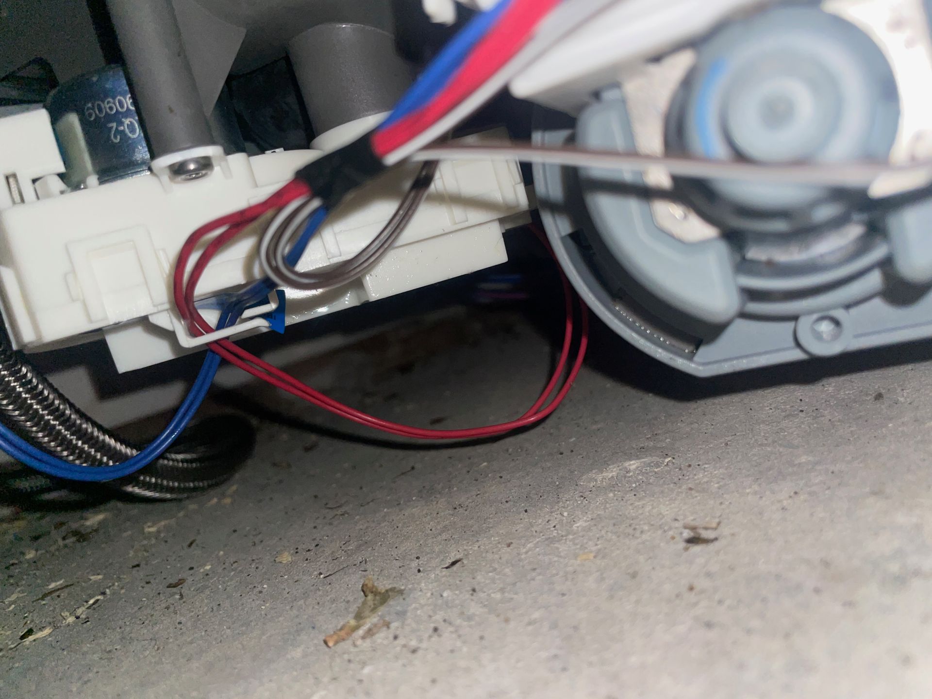 Close-up of a dishwasher's internal components, showing wiring connected to a white control box, a motor, and a gray, circular part.