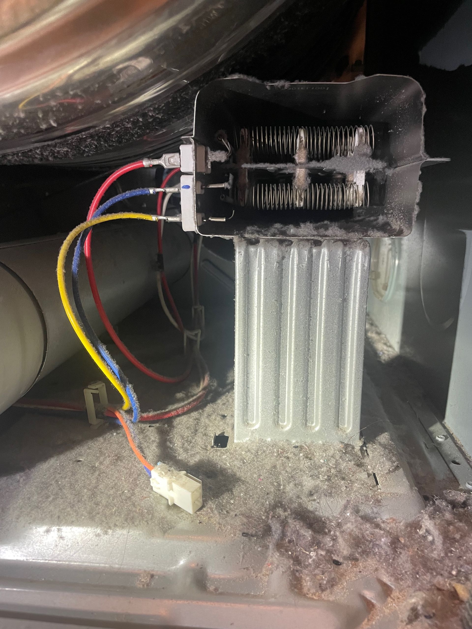 A close-up of a dryer's heating element. The element is a black rectangular box with two sets of coils, connected to wires. A white ceramic casing is below.