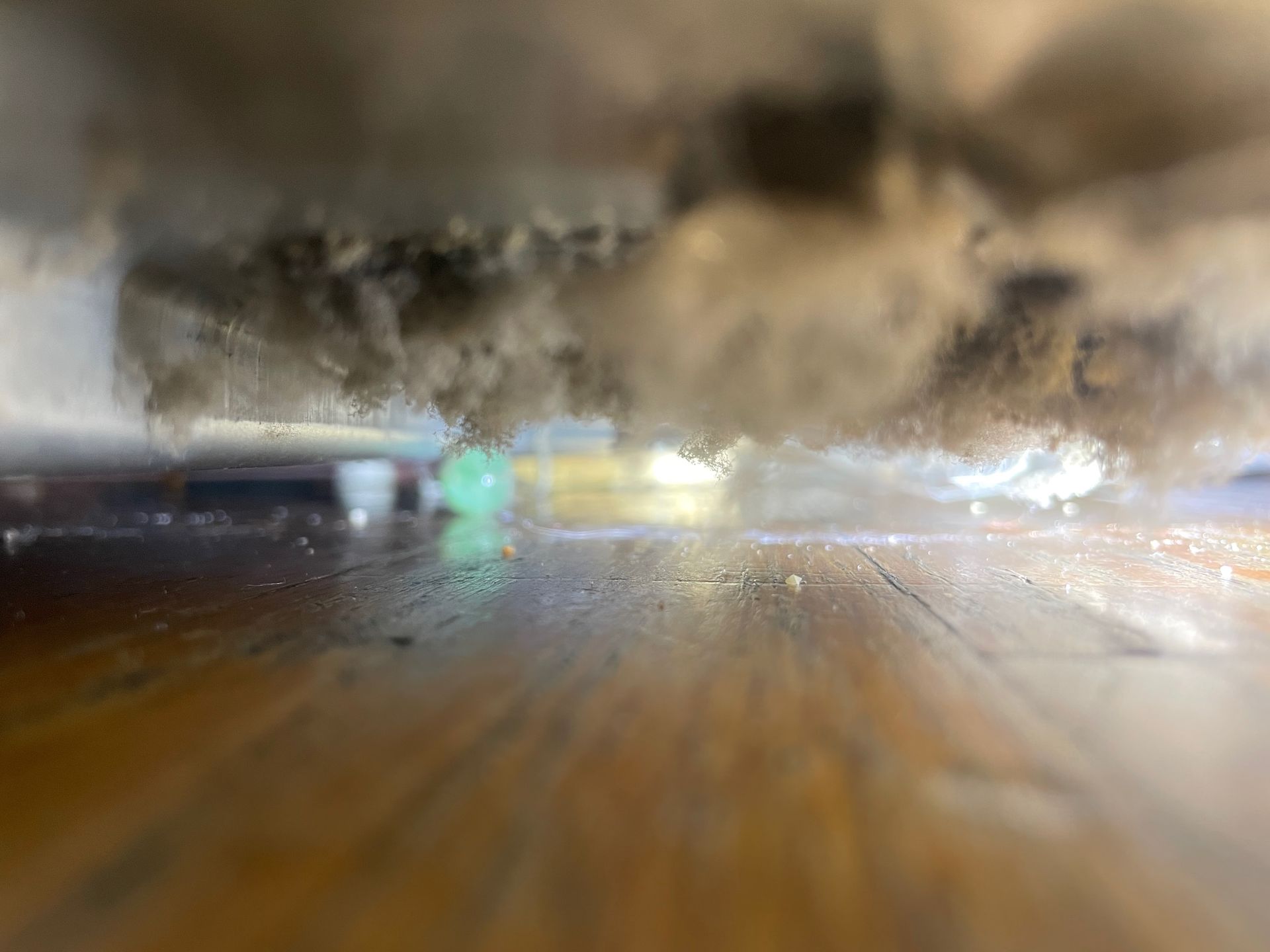 Low-angle view of a dusty surface, with a wooden floor in the foreground and a blurry, dusty mass above. A green marble is visible.
