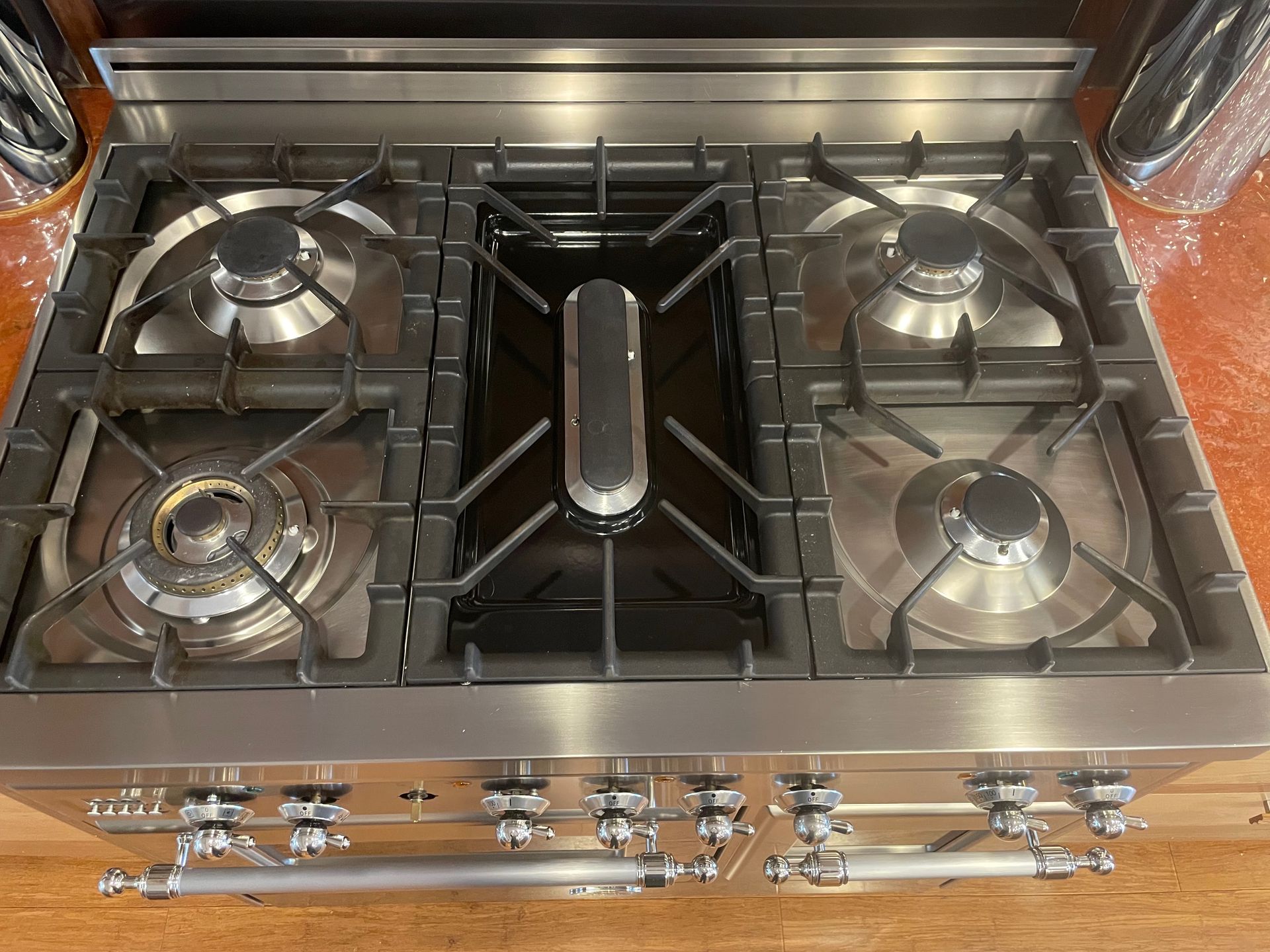 Stainless steel gas range with five burners, black grates, and silver control knobs.