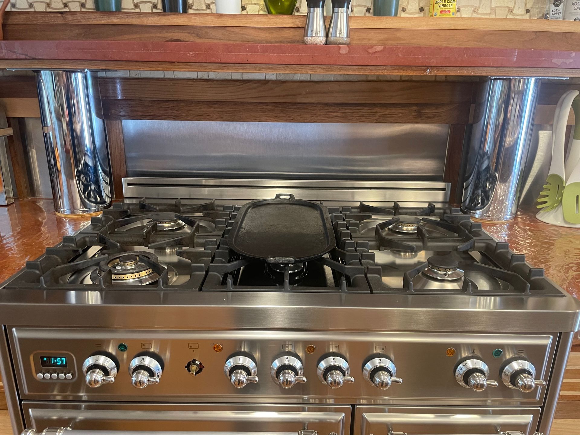 Stainless steel range with a griddle pan on the stovetop, set in a kitchen with wood and copper accents.
