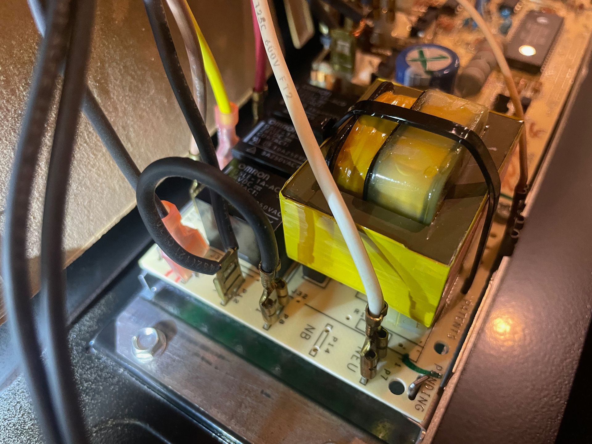 Close-up of electronic components on a circuit board with a black and yellow transformer. Wires connect to terminals.