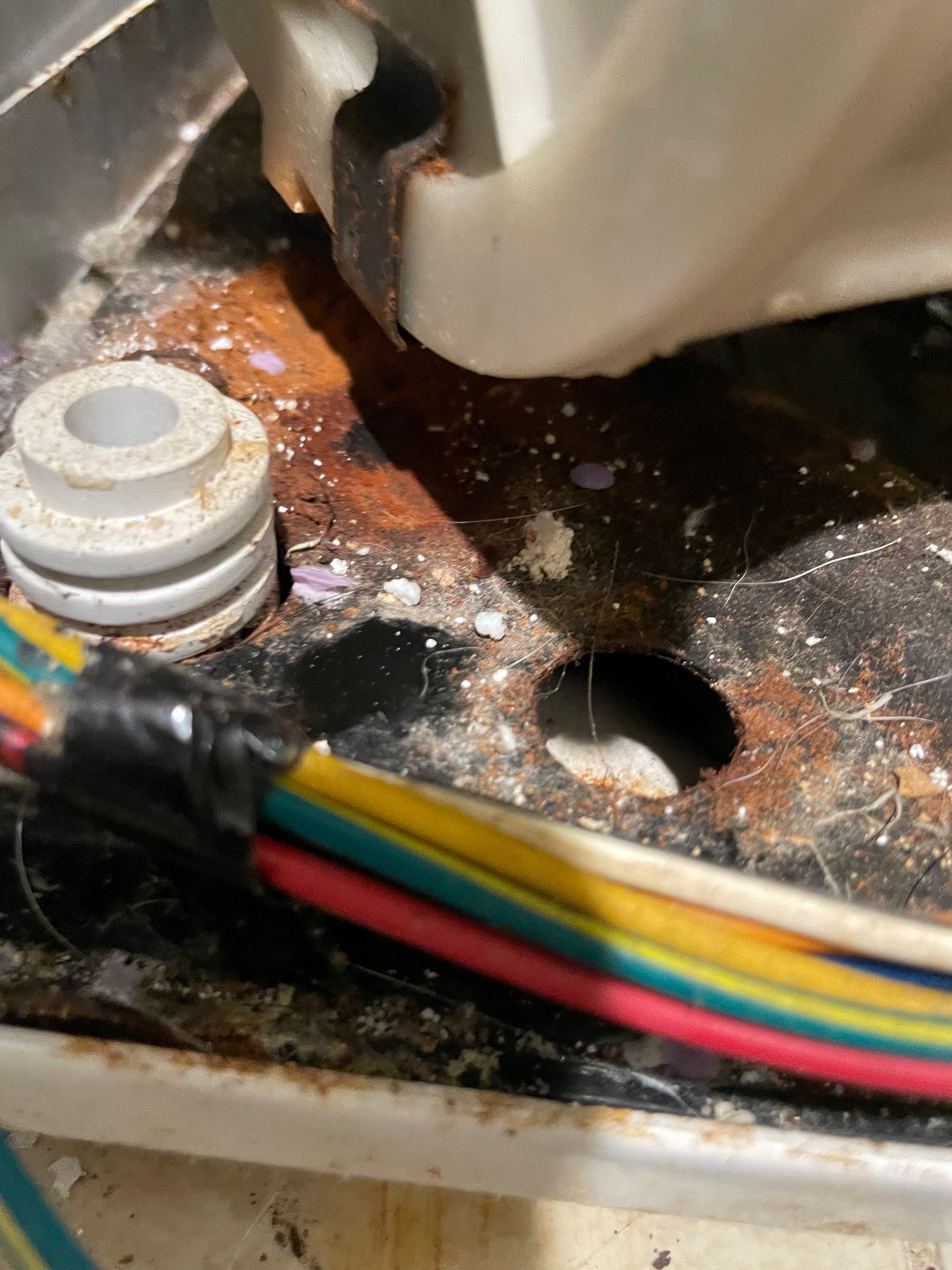 Close-up of rusty metal base with wires and a white plastic component. A hole is visible.