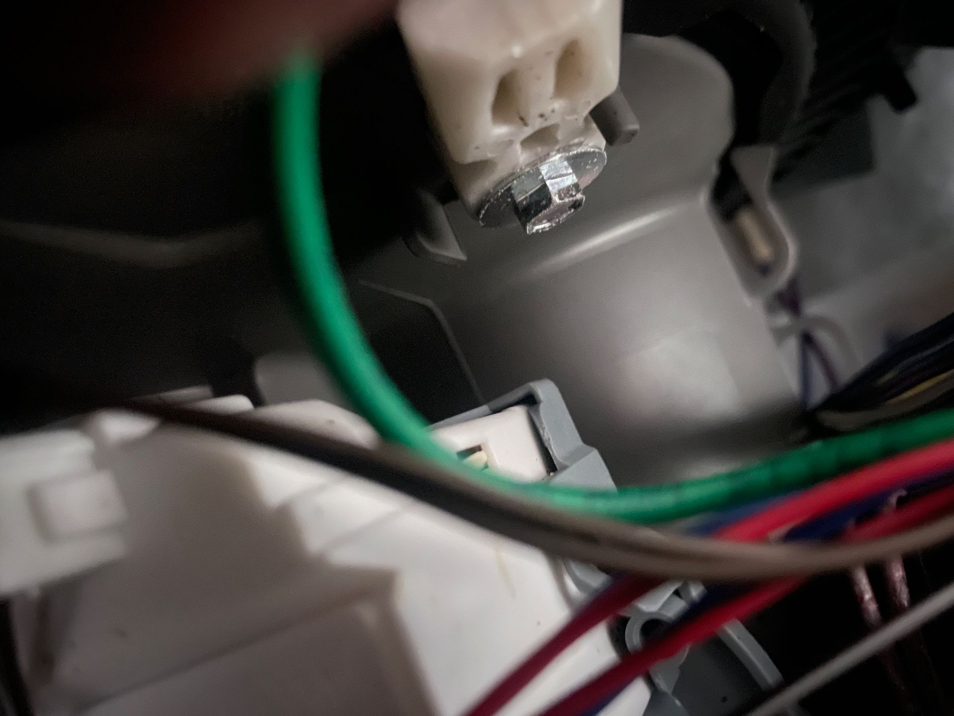 Close-up of electrical wiring connections: white and grey plugs, green and other colored wires.  A bolt is covered with what appears to be foil.