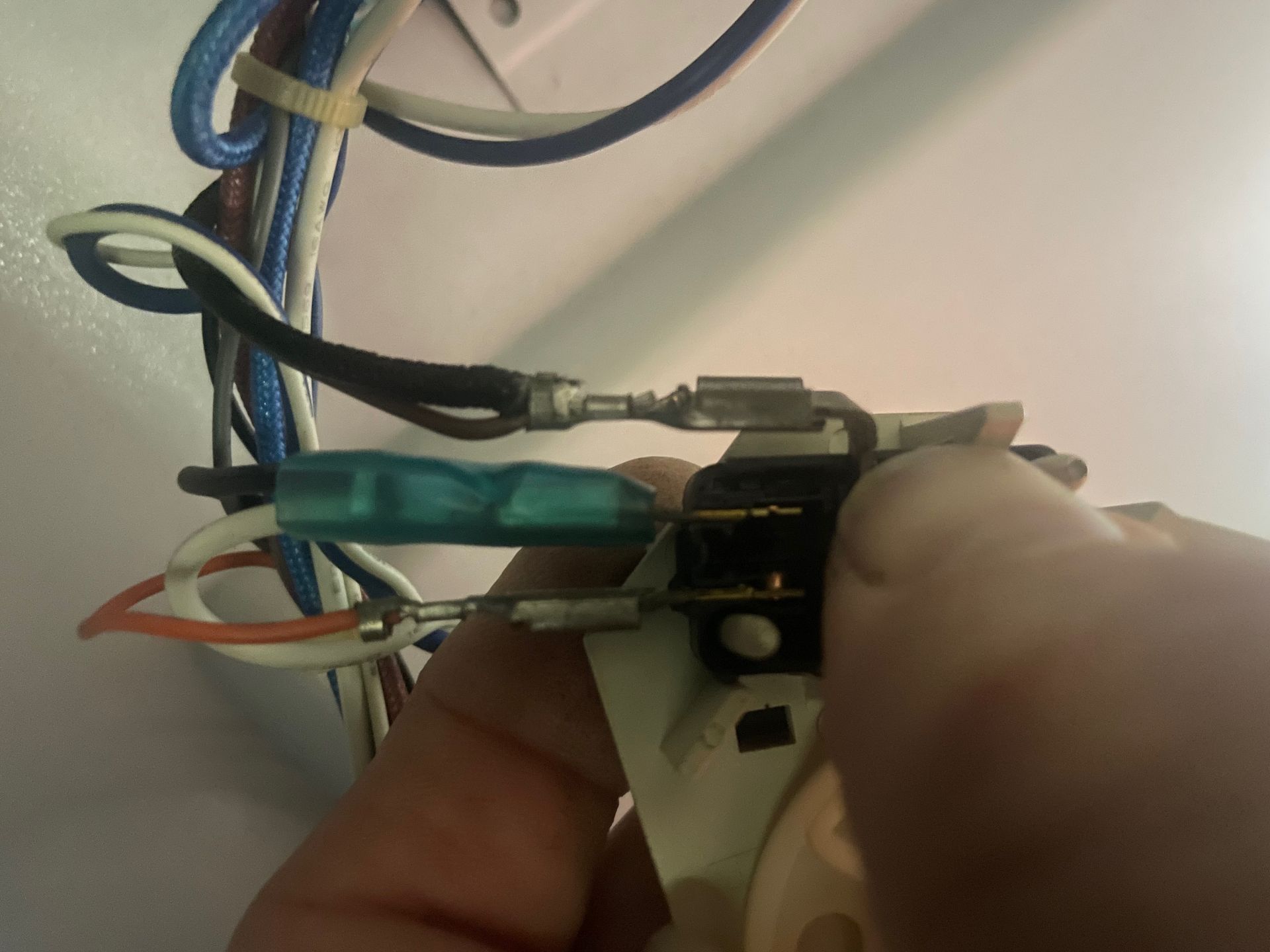 Hand touching a switch with attached wires inside an appliance. Various colored wires are connected to the switch.