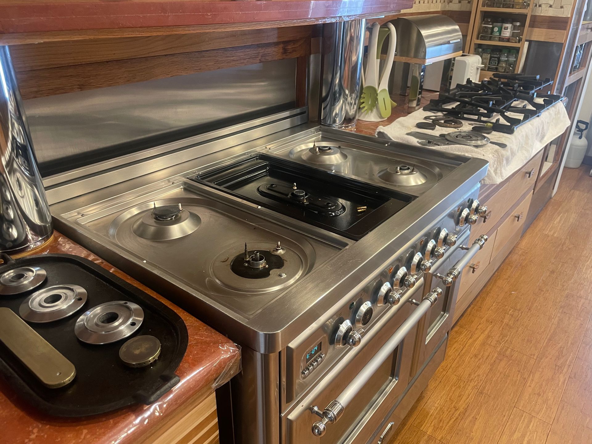 A stainless steel stove in a kitchen setting with burners and a black griddle. Parts are on a tray to the side.