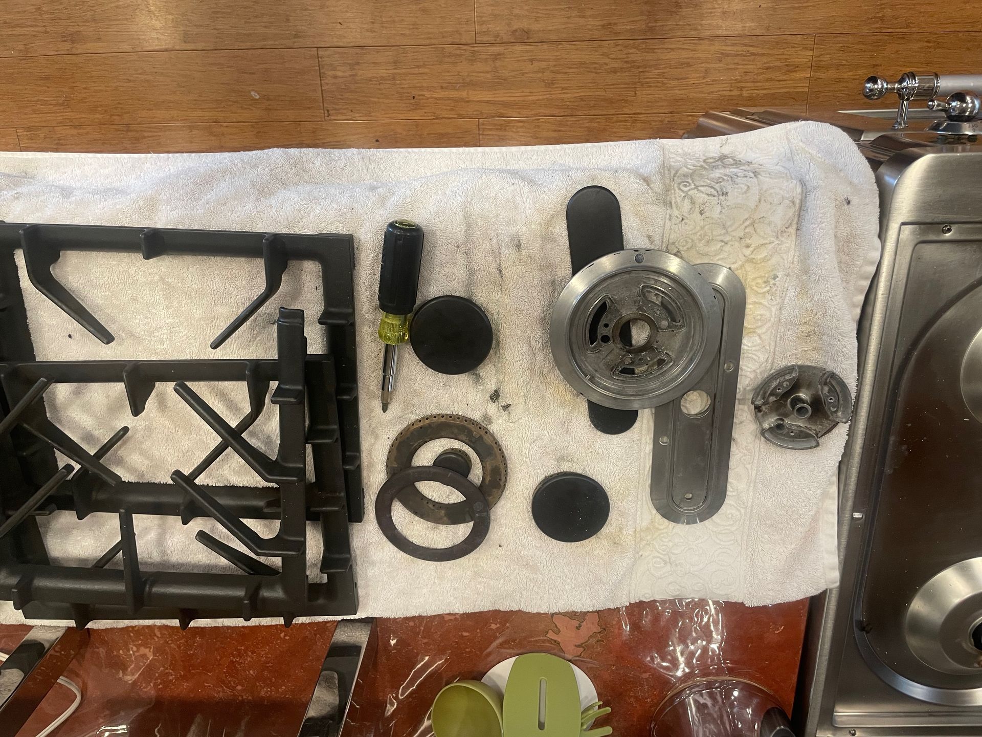 Overhead view of stove parts on a white towel: grates, burner caps, a screwdriver, and other disassembled components.