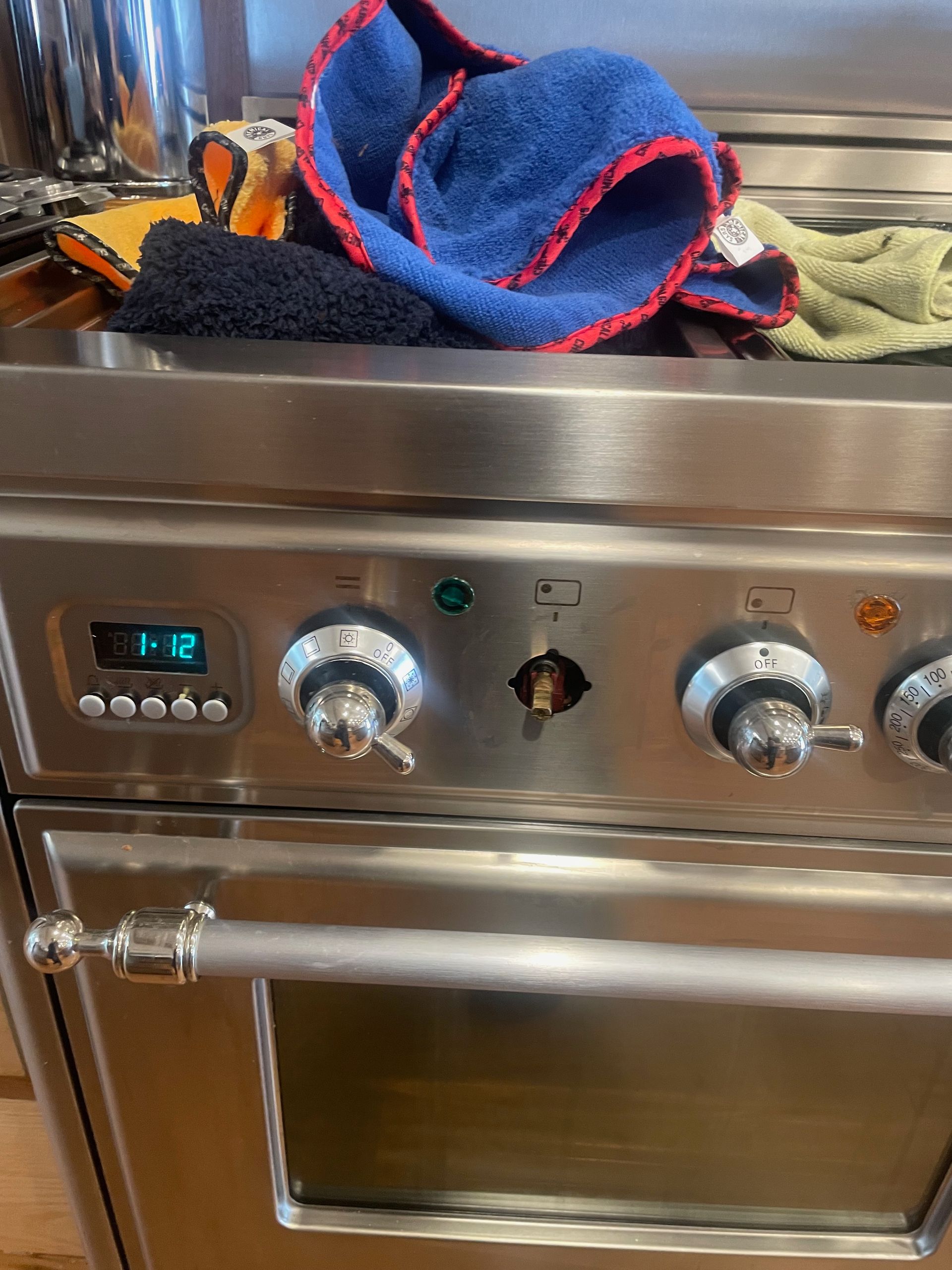 Stainless steel stove with a missing knob, digital display, and various cleaning cloths on top.