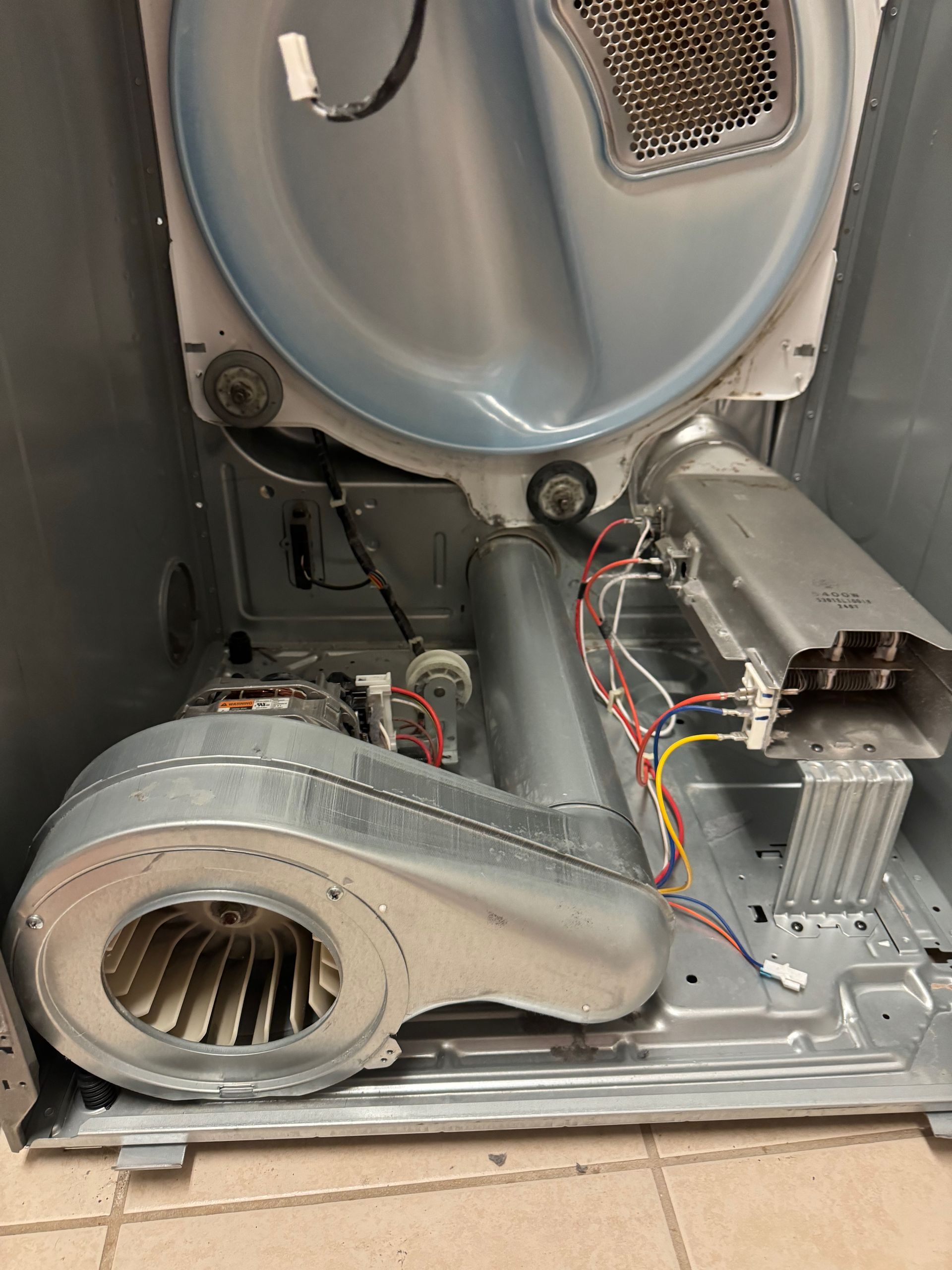 Interior of a gray dryer showing the drum, blower fan, heating element, and wiring.