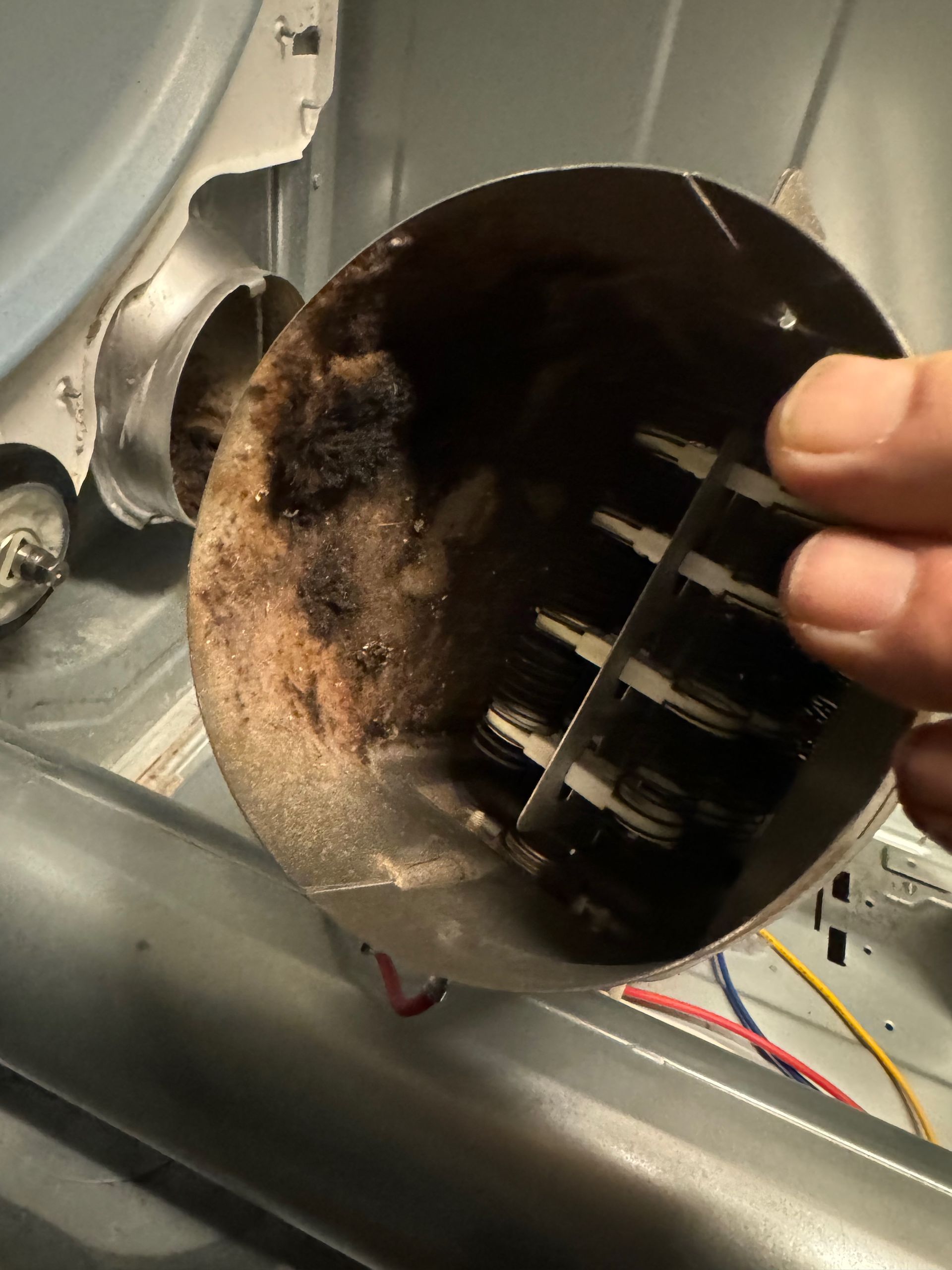 Close-up of a dryer's lint trap housing, filled with black, charred lint. A hand holds the trap.