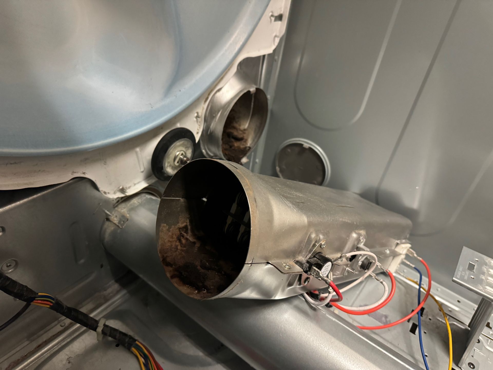 Interior view of a disassembled dryer, showing a rusty heating element and lint buildup.