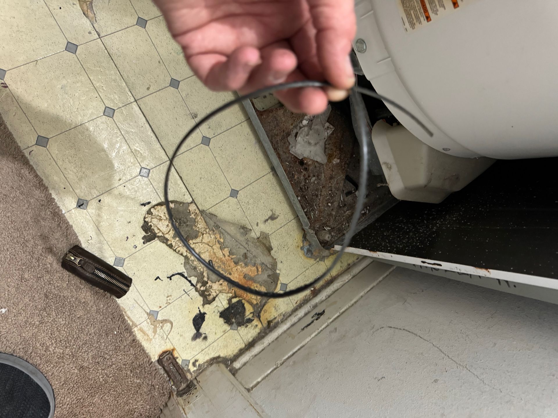 A person holds a black circular rubber seal next to a washing machine in a room with damaged flooring.