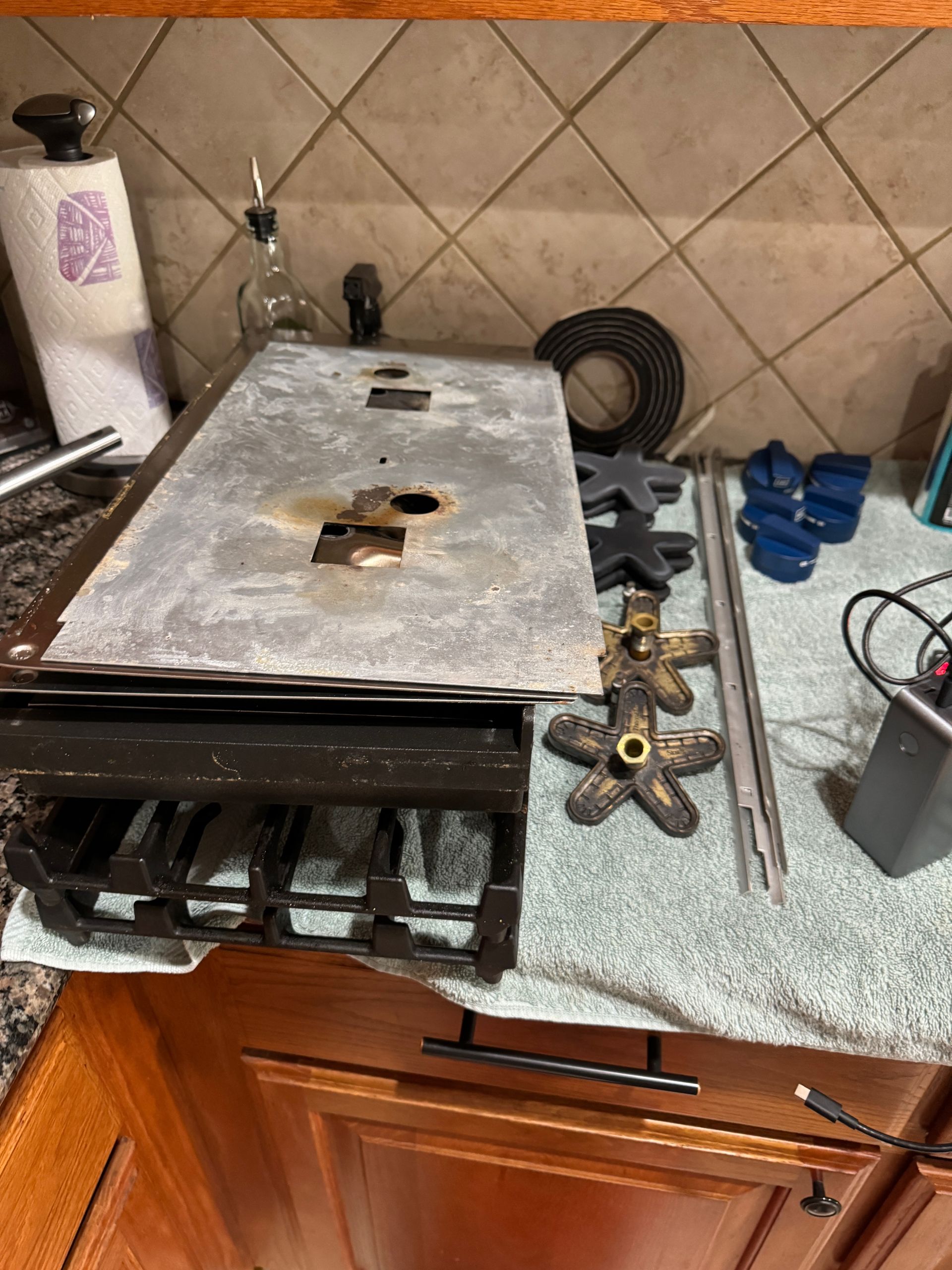 Disassembled stove top with grates, burners, and other parts on a countertop. Kitchen setting.
