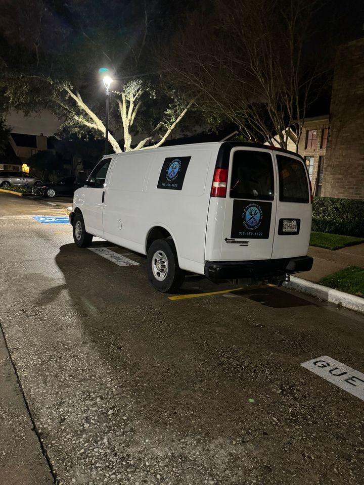 White cargo van parked on an asphalt lot, illuminated by a street light at night. Van has black graphics on the back doors.