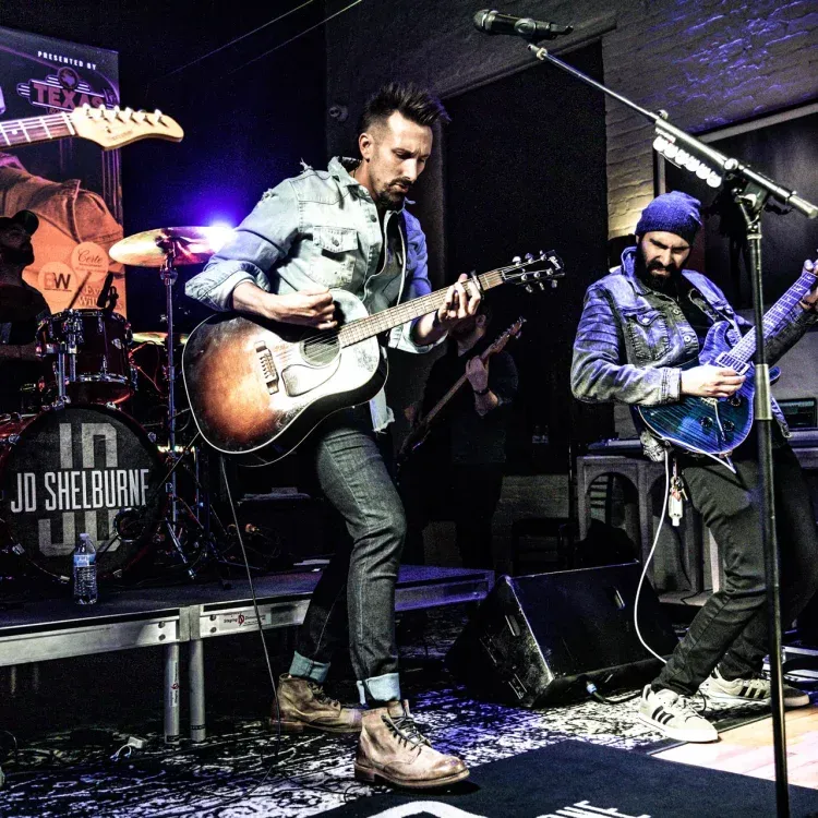 A man playing a guitar in front of a sign that says jd shelburne