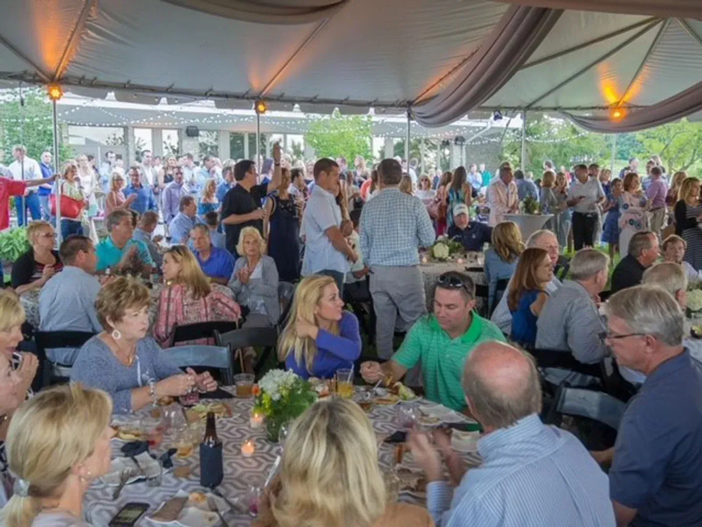 A large group of people are sitting at tables under a tent.