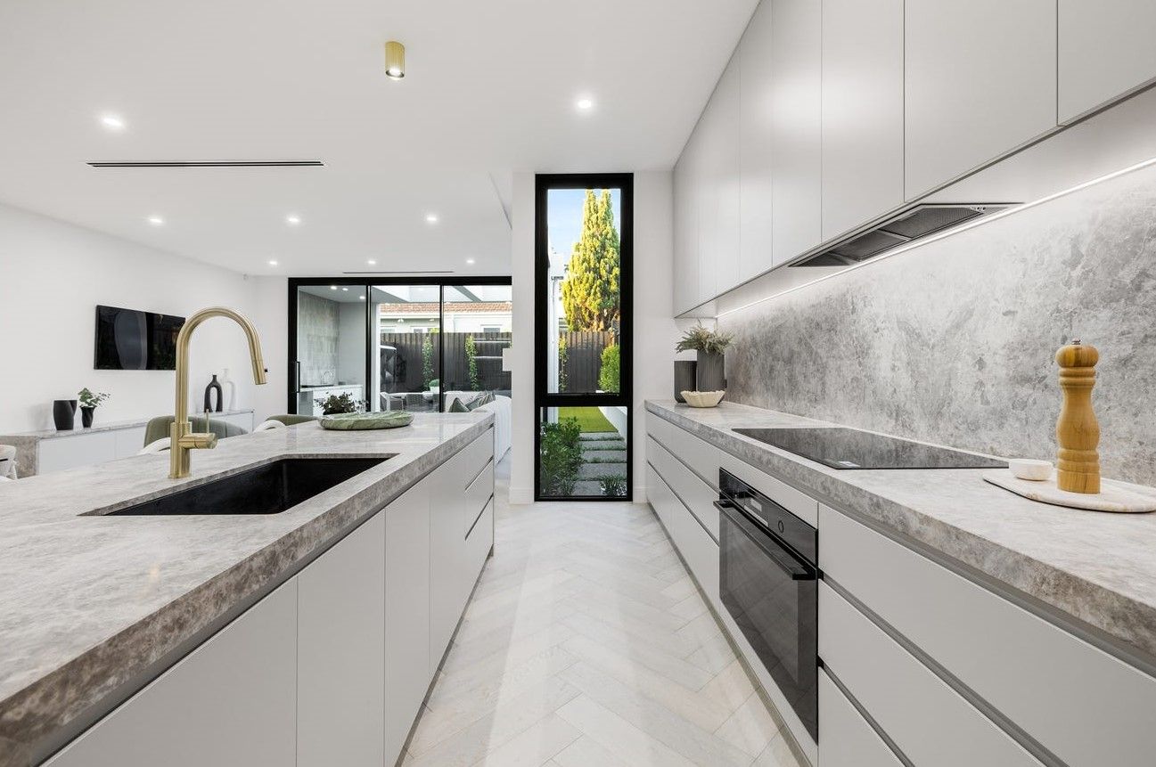 Modern, white kitchen with gray countertops and a black sink, overlooking a backyard.